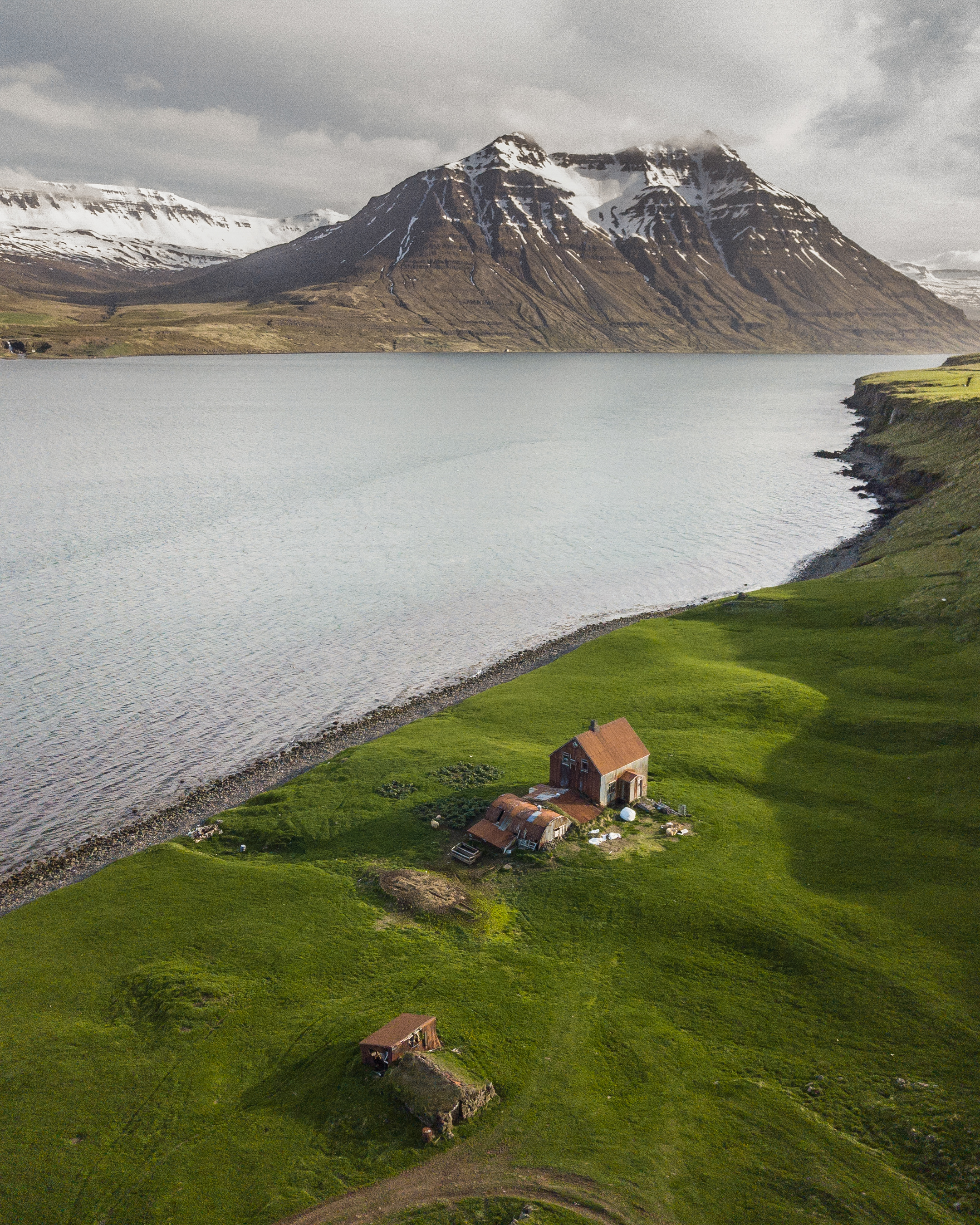 Remote farm buildings beside a long Eastfjords shoreline and mountain basin