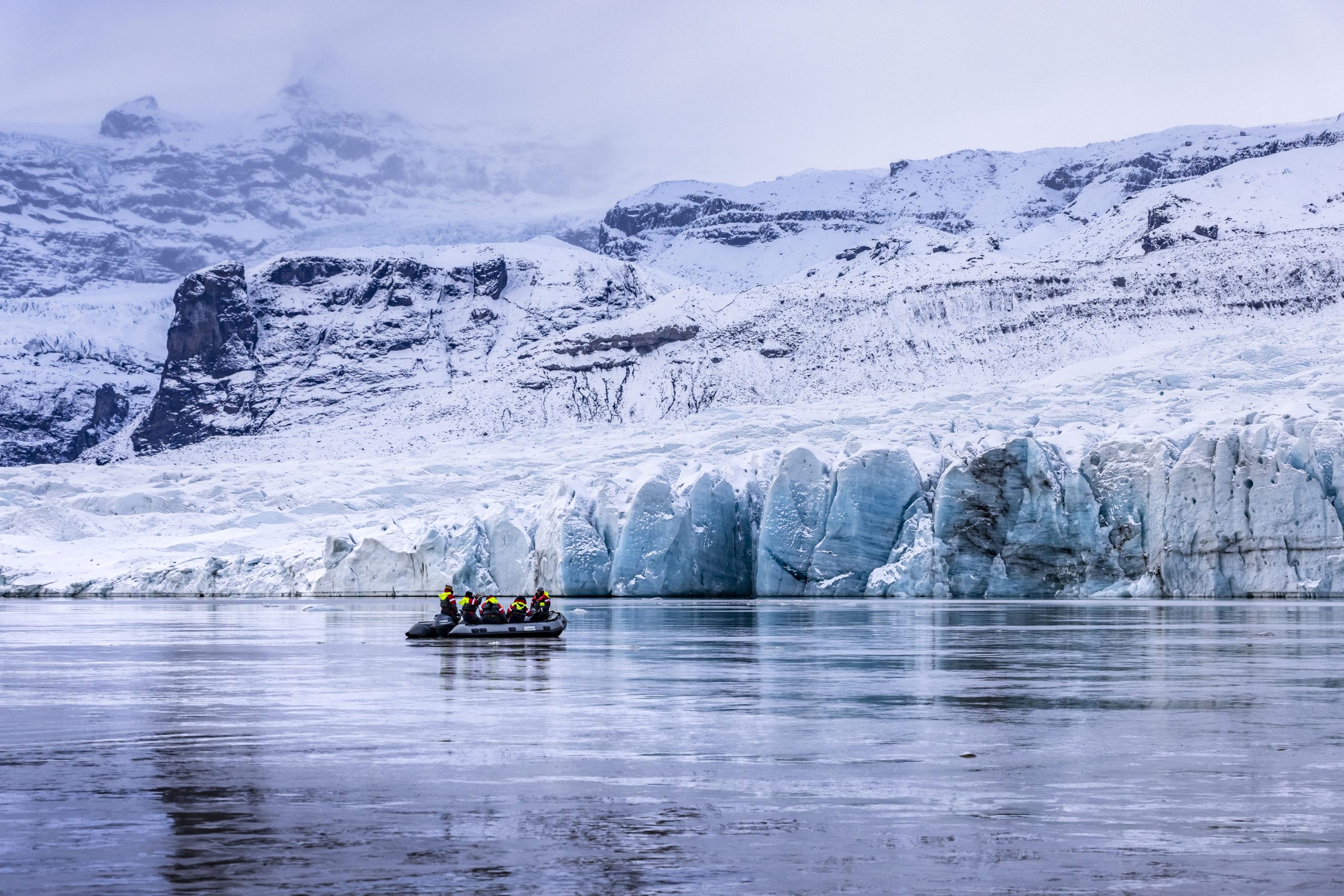 Small Zodiac carrying passengers beneath a snowy glacier at Fjallsárlón