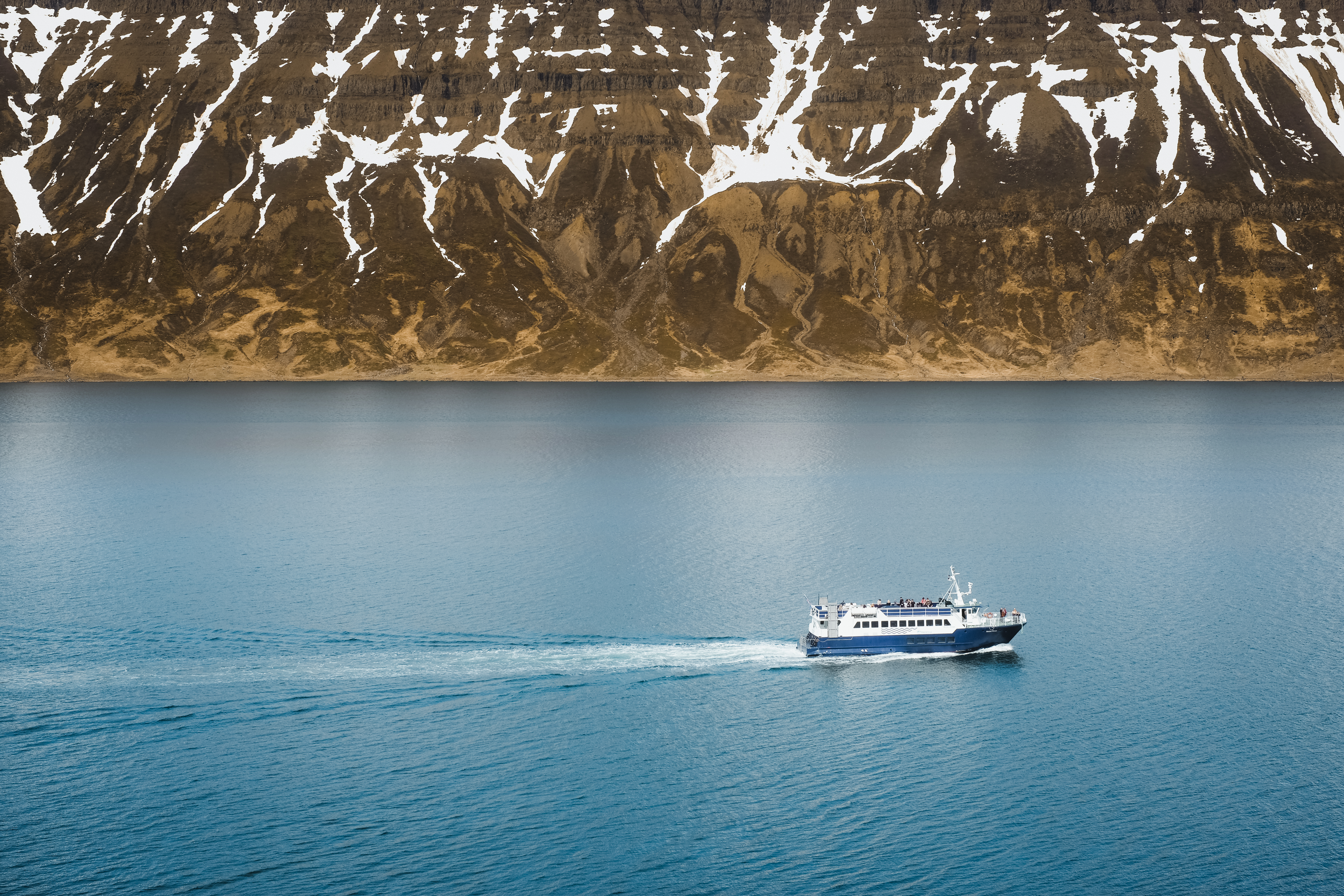 Passenger ship crossing a broad Eastfjords fjord beneath snow-streaked mountains