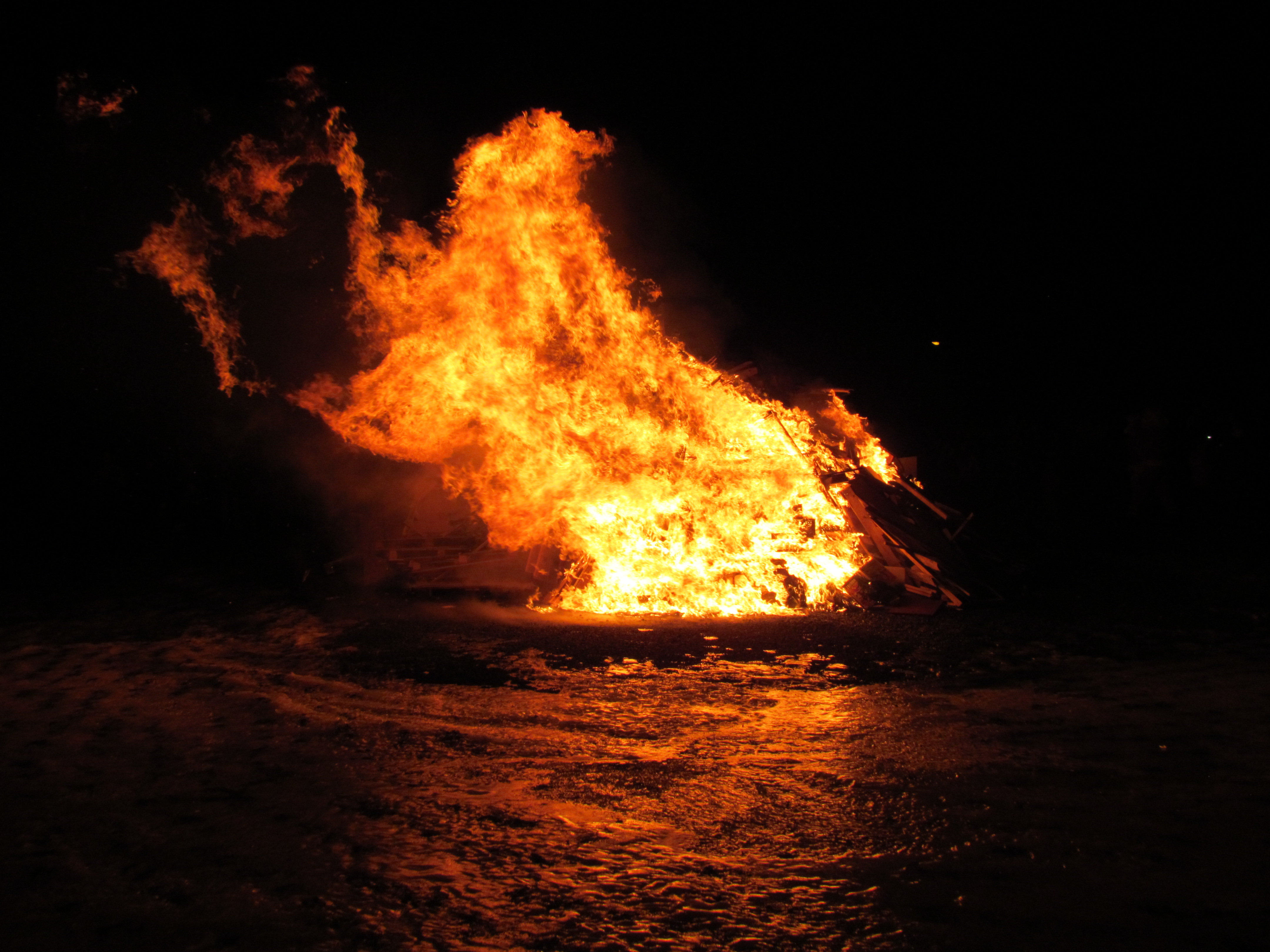 Large Icelandic New Year bonfire burning on snow under a dark night sky