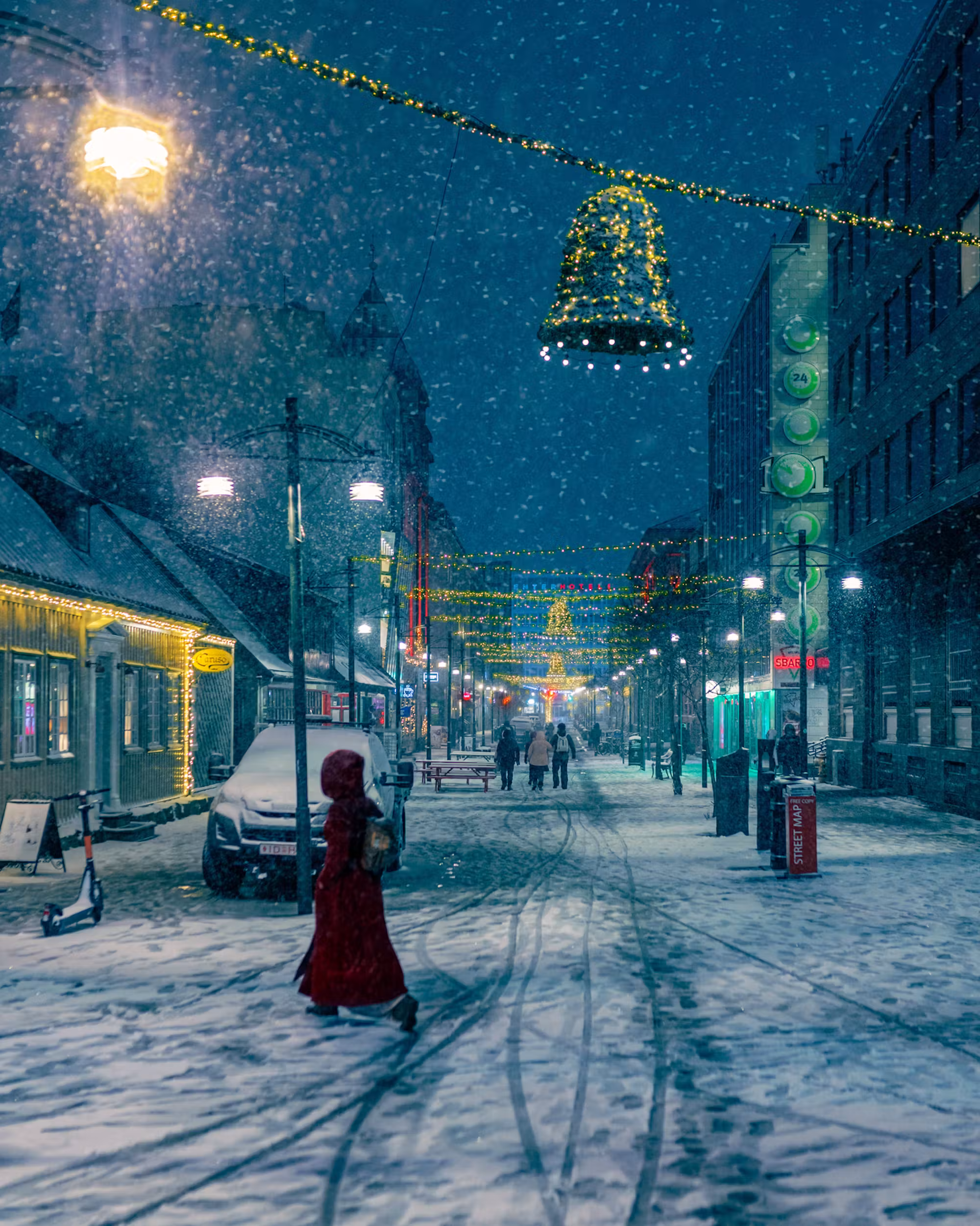 A few pedestrians on snow-covered Austurstræti beneath illuminated Christmas bell decorations