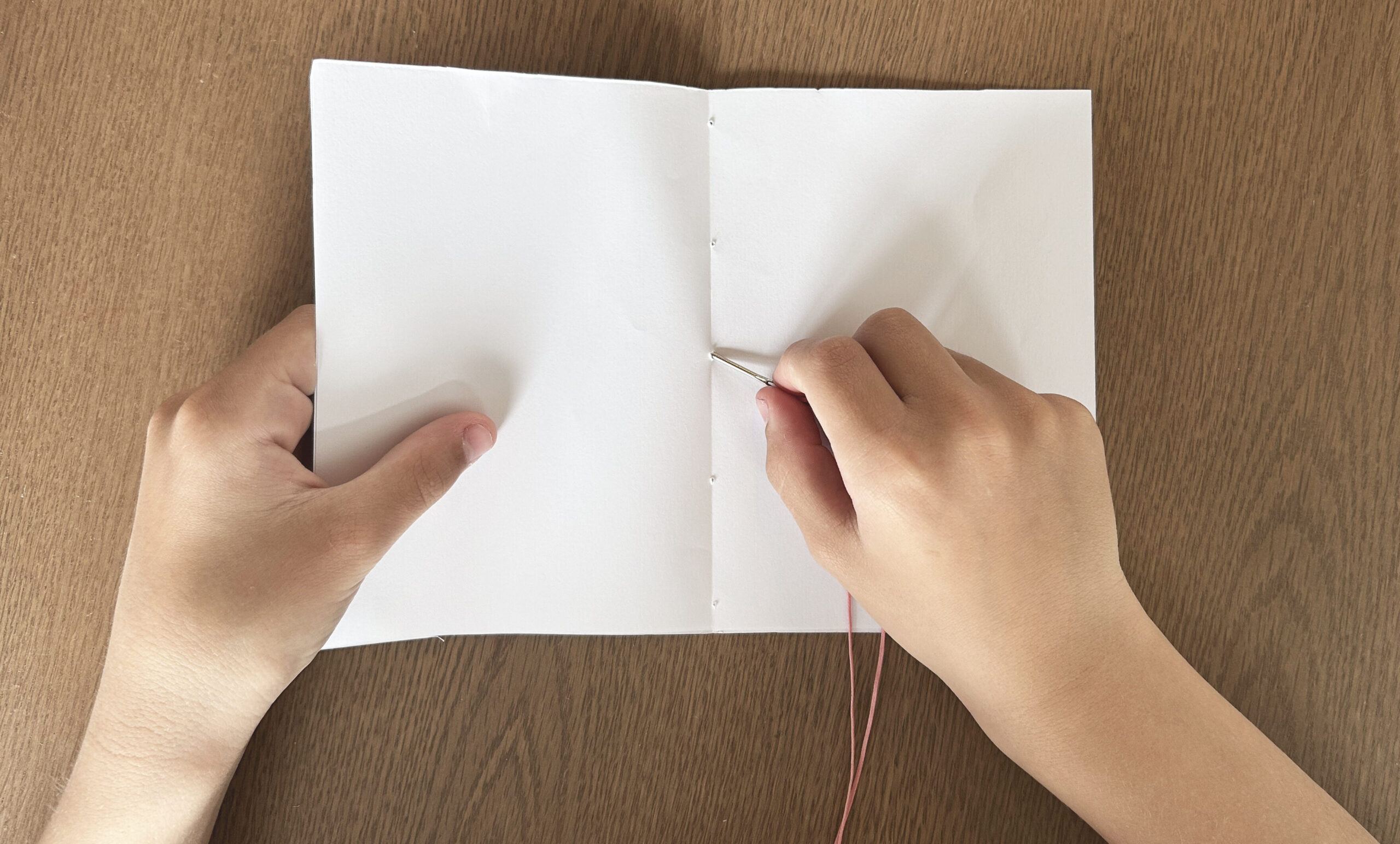 Hands stitching folded paper into a book with needle and thread