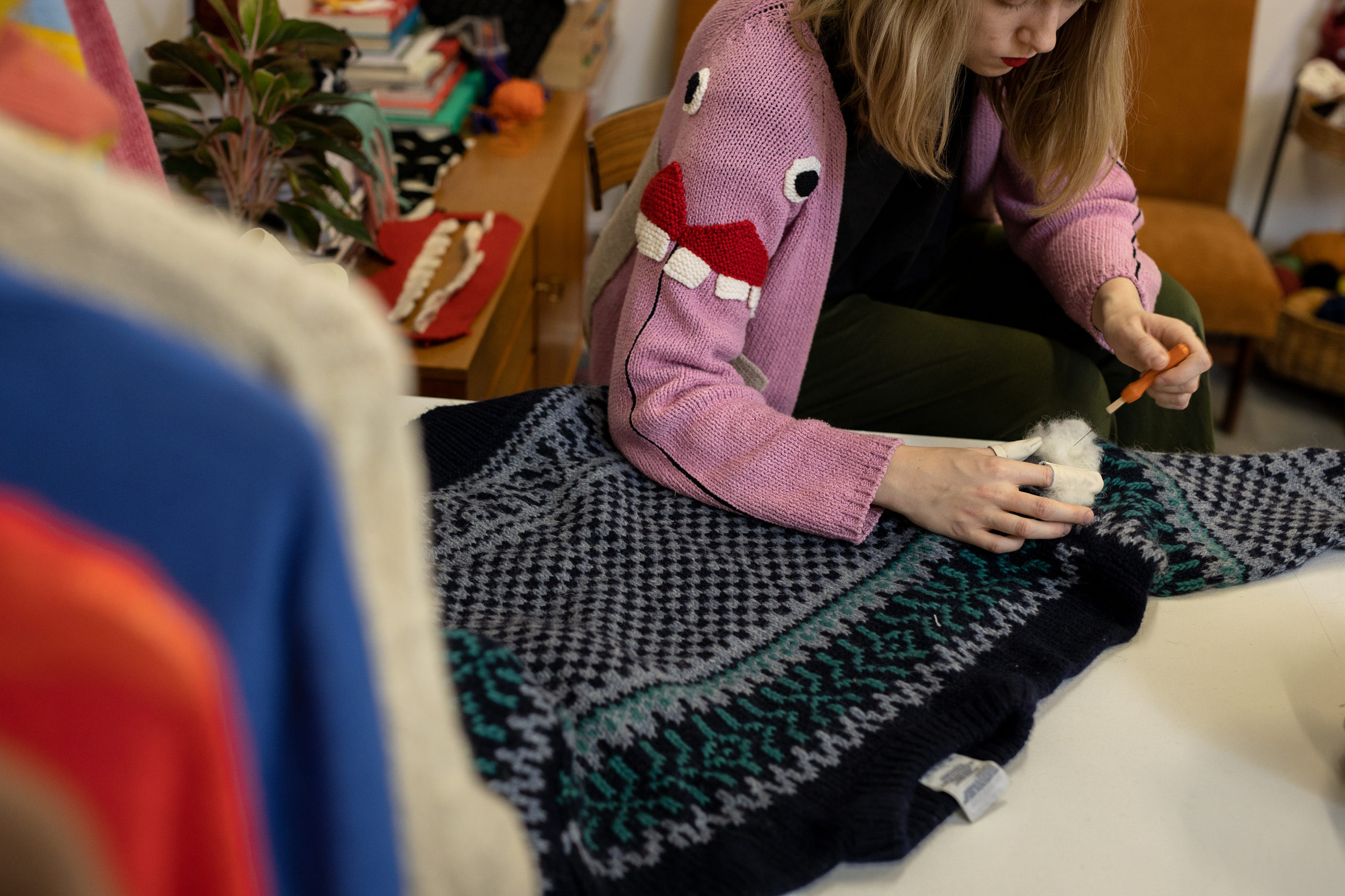 Textile maker needle-felting a patterned wool sweater on a worktable