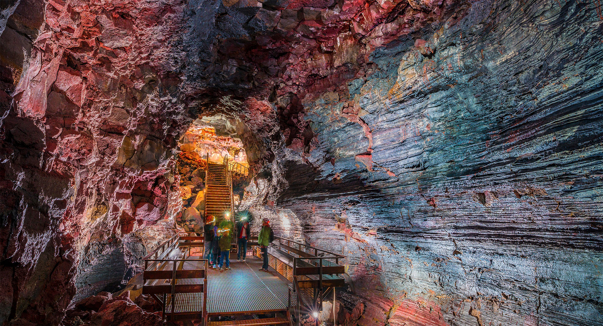 Visitors on a metal platform beneath the layered rock walls of Raufarhólshellir lava tunnel