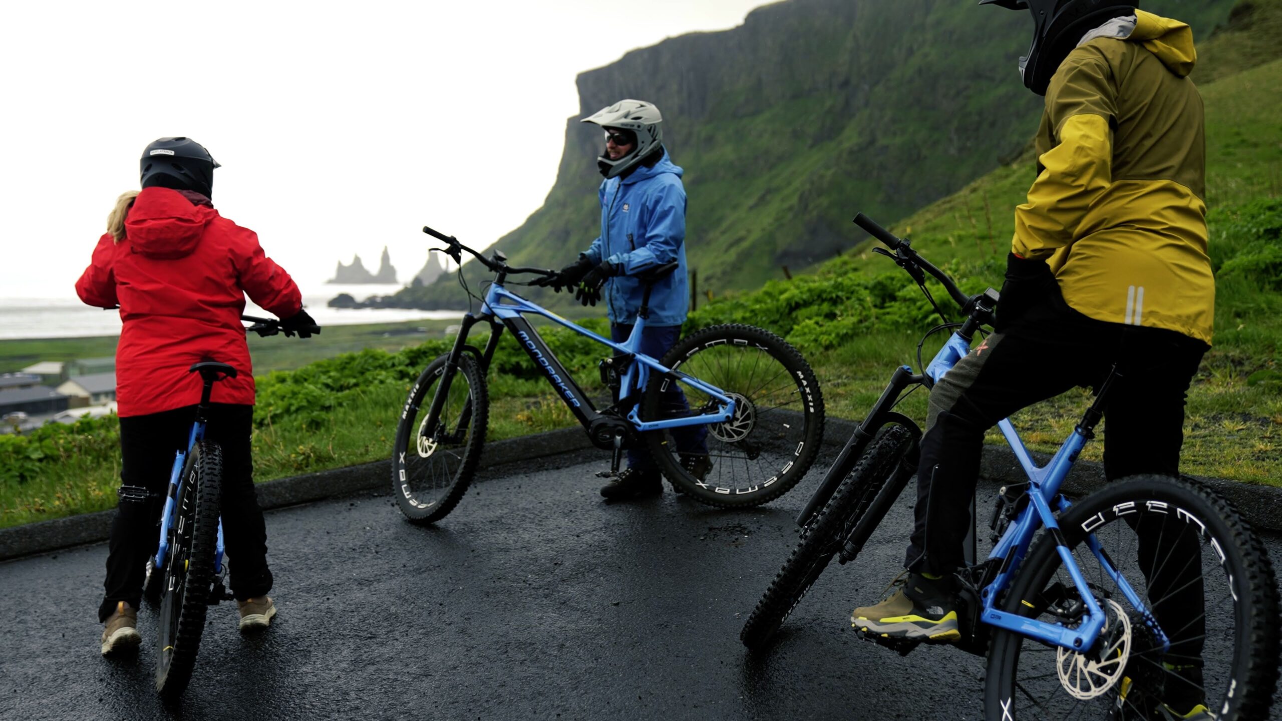 Guide and electric mountain bikers wearing rain layers near Vík