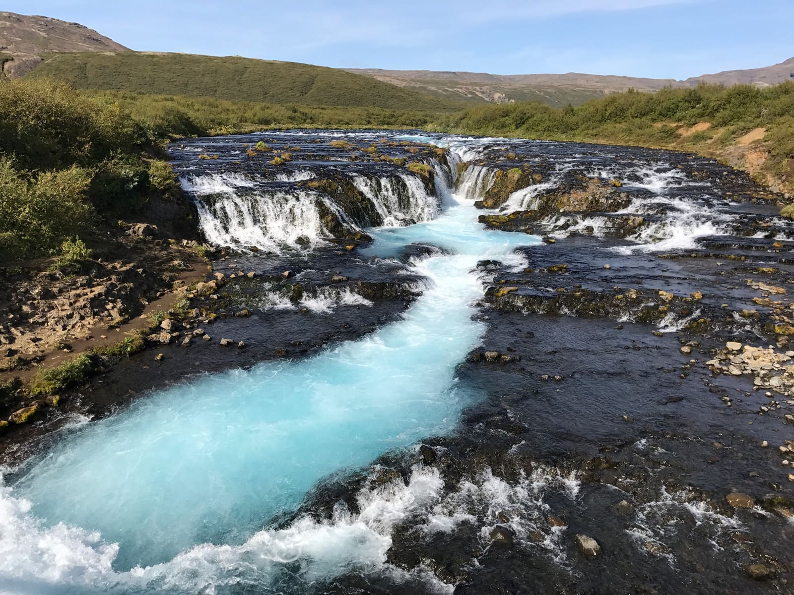 Blue water flowing over the dark rock steps of Brúarfoss on Iceland's Golden Circle.