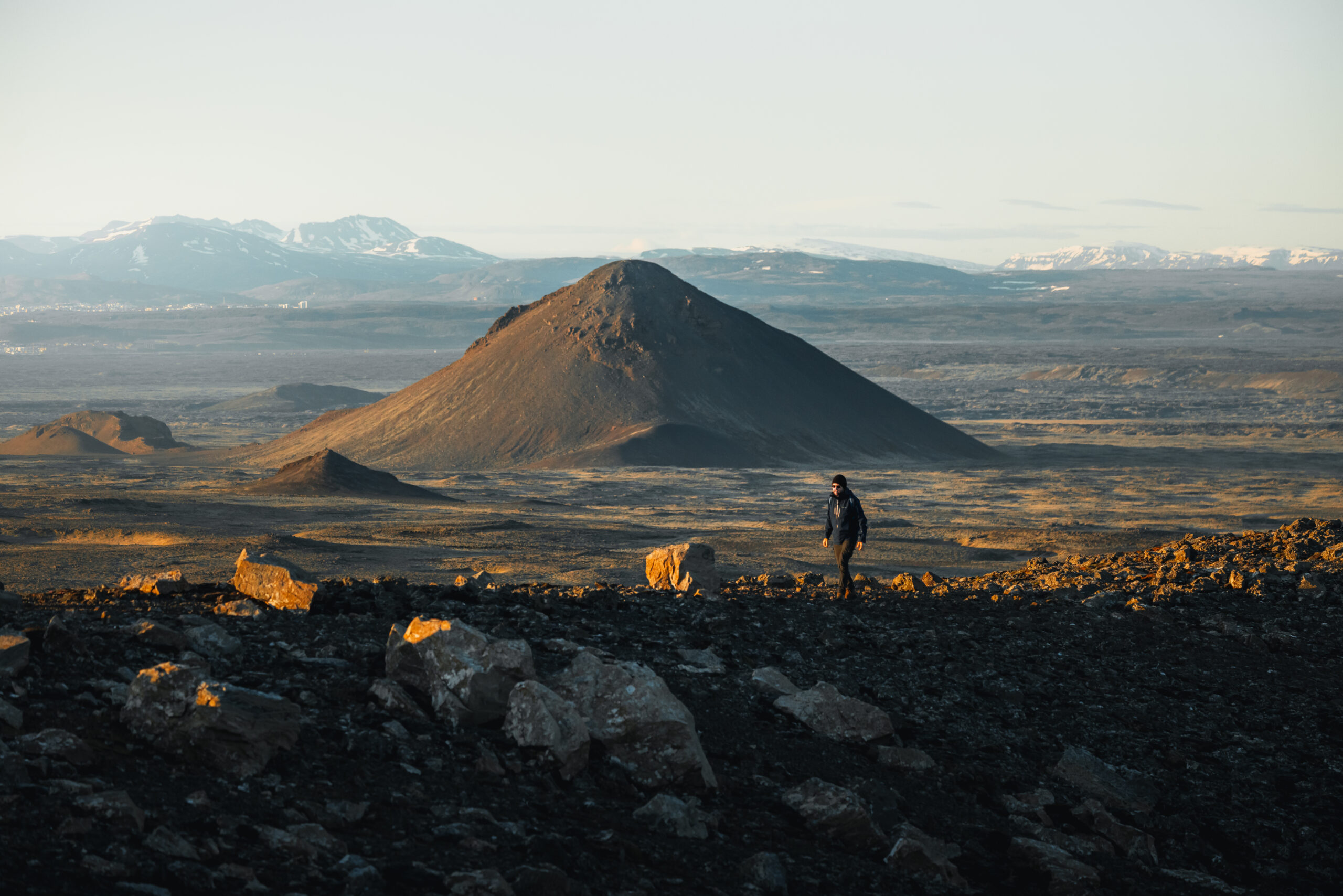 A lone hiker crossing broad cooled lava terrain near Fagradalsfjall on the Reykjanes Peninsula.