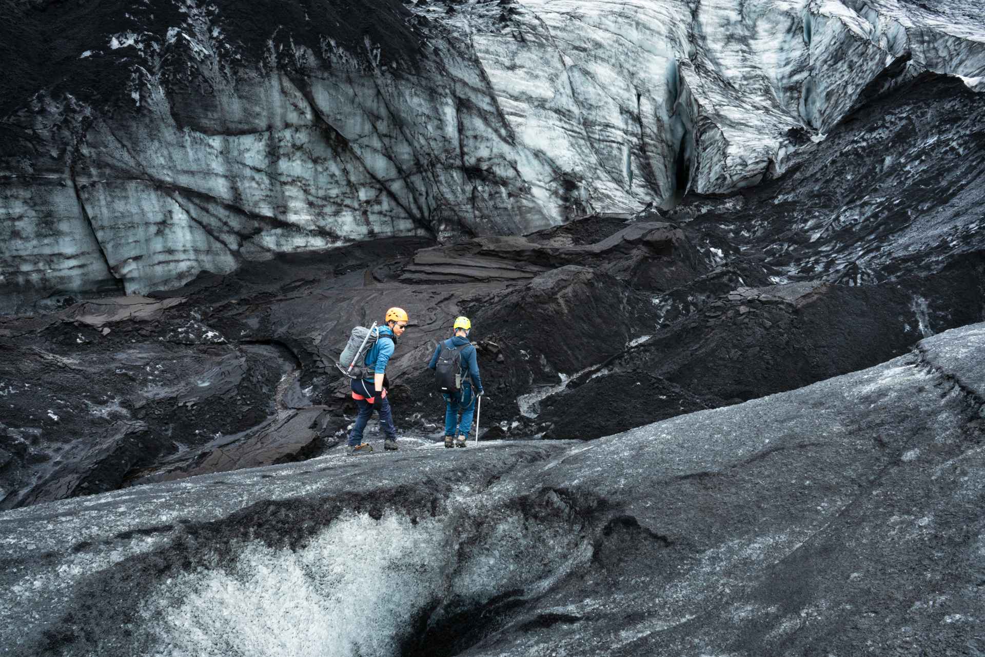 Two helmeted hikers crossing the dark ridged ice of Sólheimajökull glacier on Iceland's South Coast.