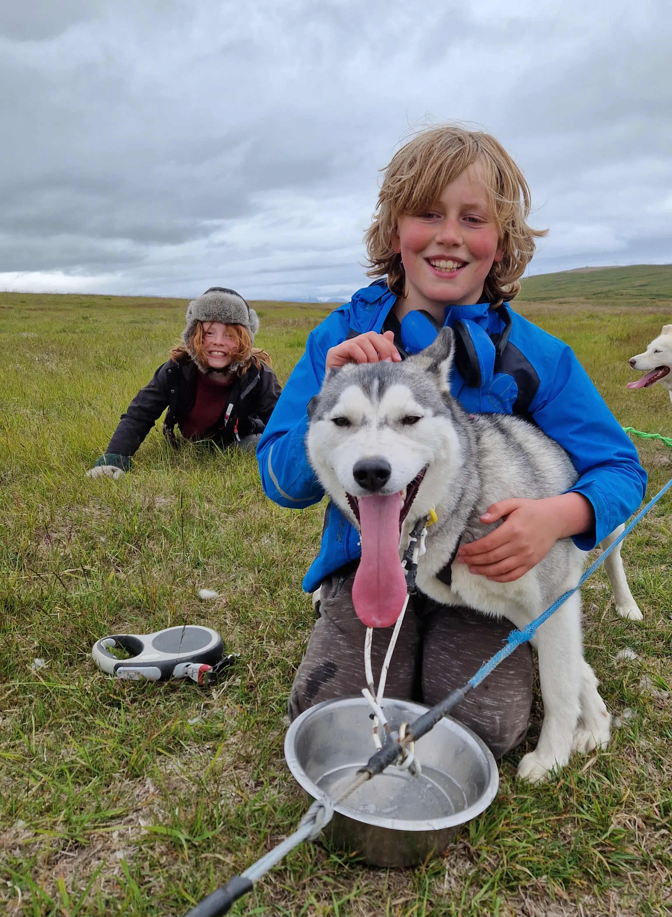 Child sitting beside a resting husky with a water bowl after a dry-land outing
