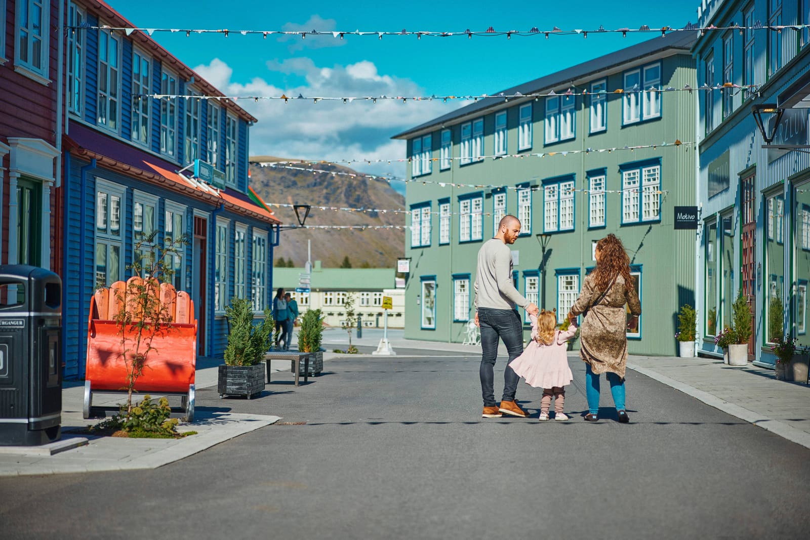 Two adults walking hand in hand with a young child along a colorful Icelandic town street