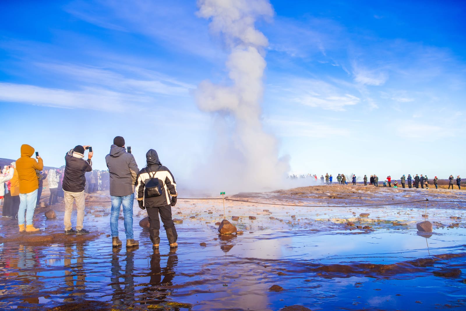 Travelers watching Strokkur erupt from the marked viewing area