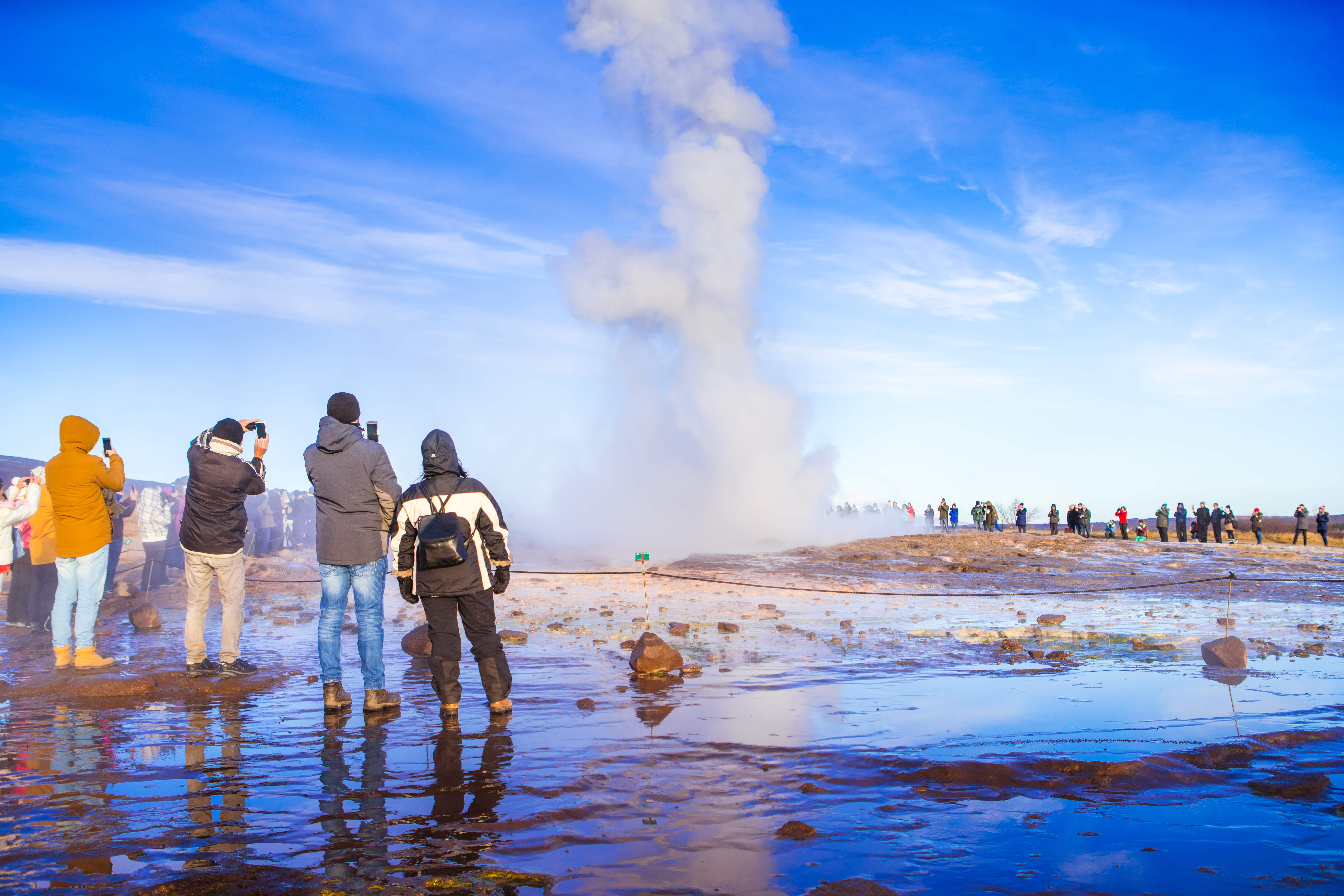 Visitors watching Strokkur erupt from behind the marked geothermal viewing boundary
