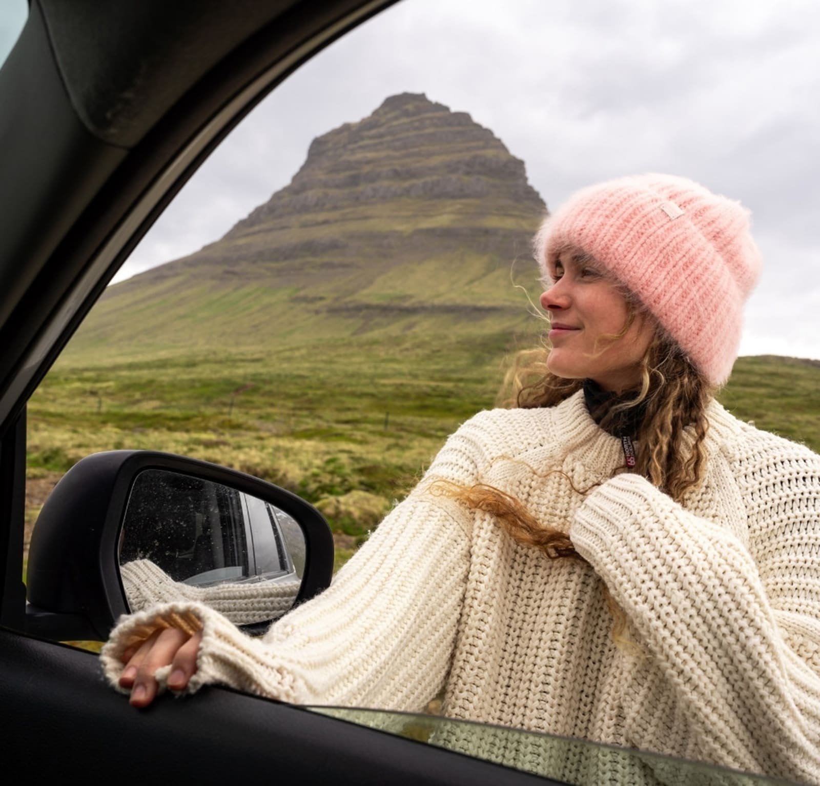 Traveler beside a car with Kirkjufell mountain behind her in Snæfellsnes