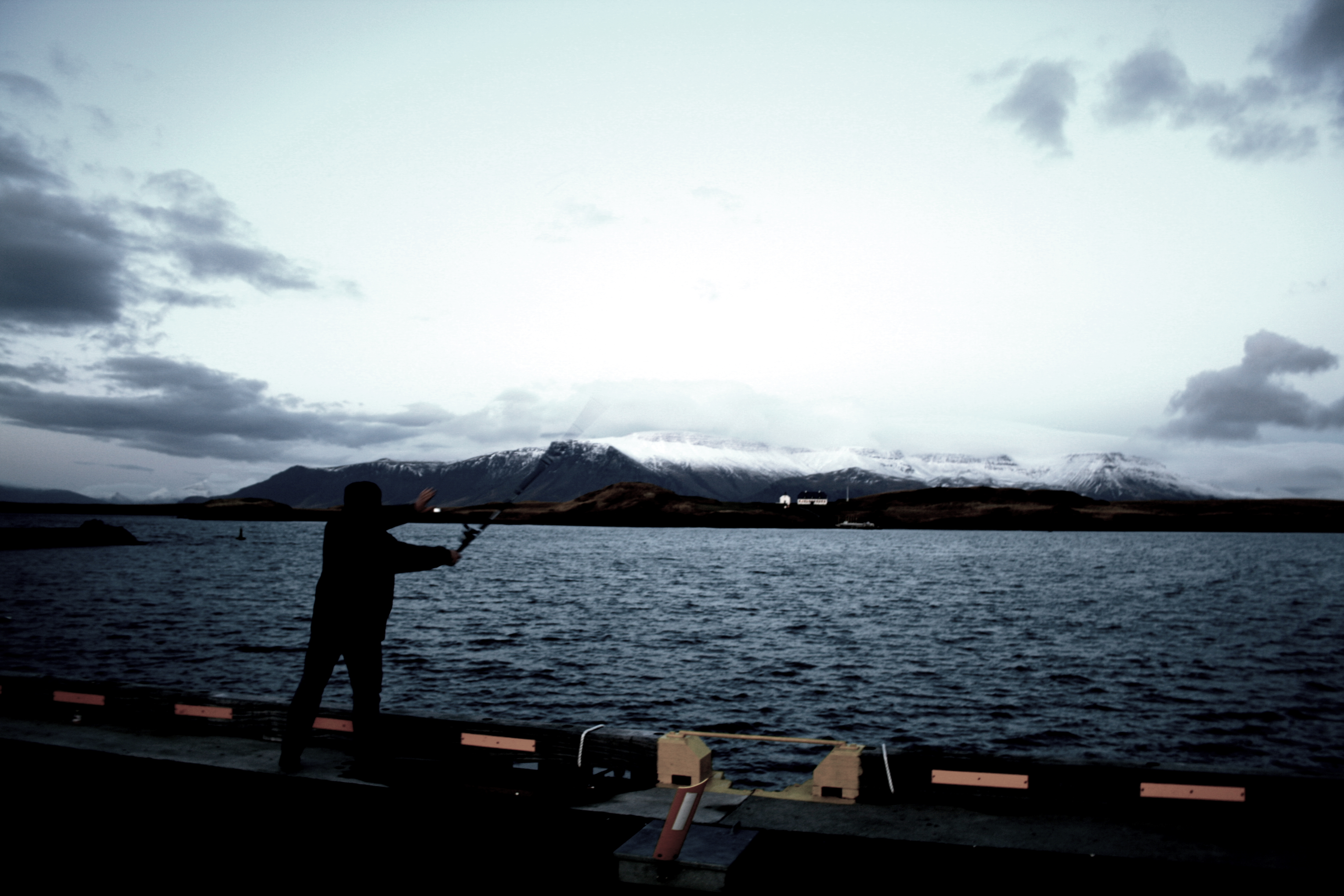 Silhouetted angler casting across an Icelandic lake below snowy mountains