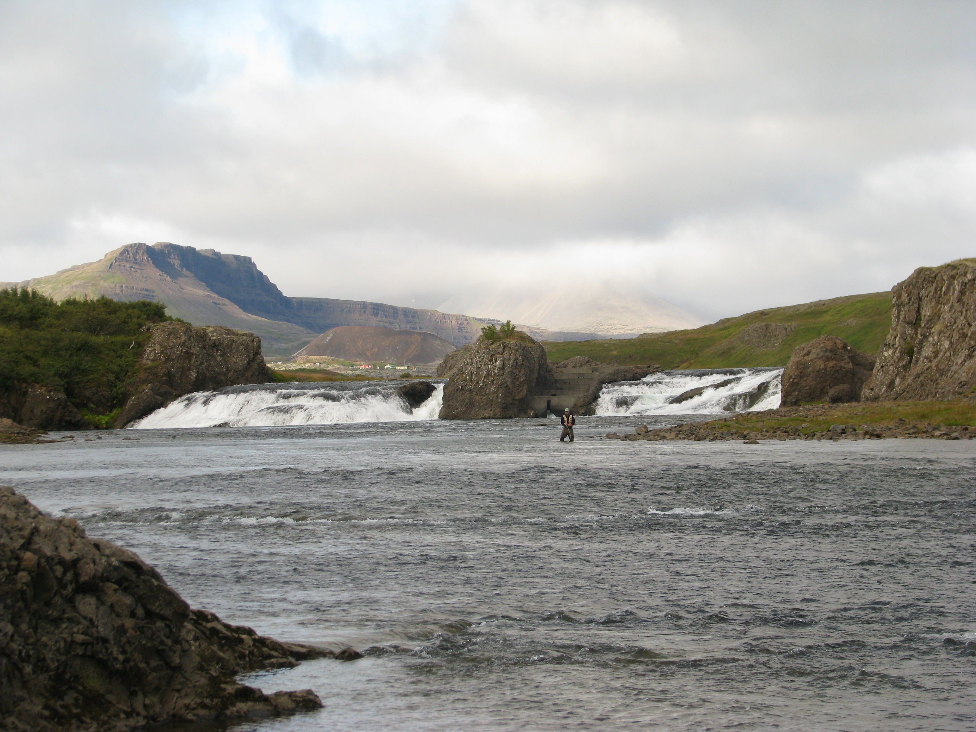 Angler wading below Laxfoss with mountains and broken river channels behind