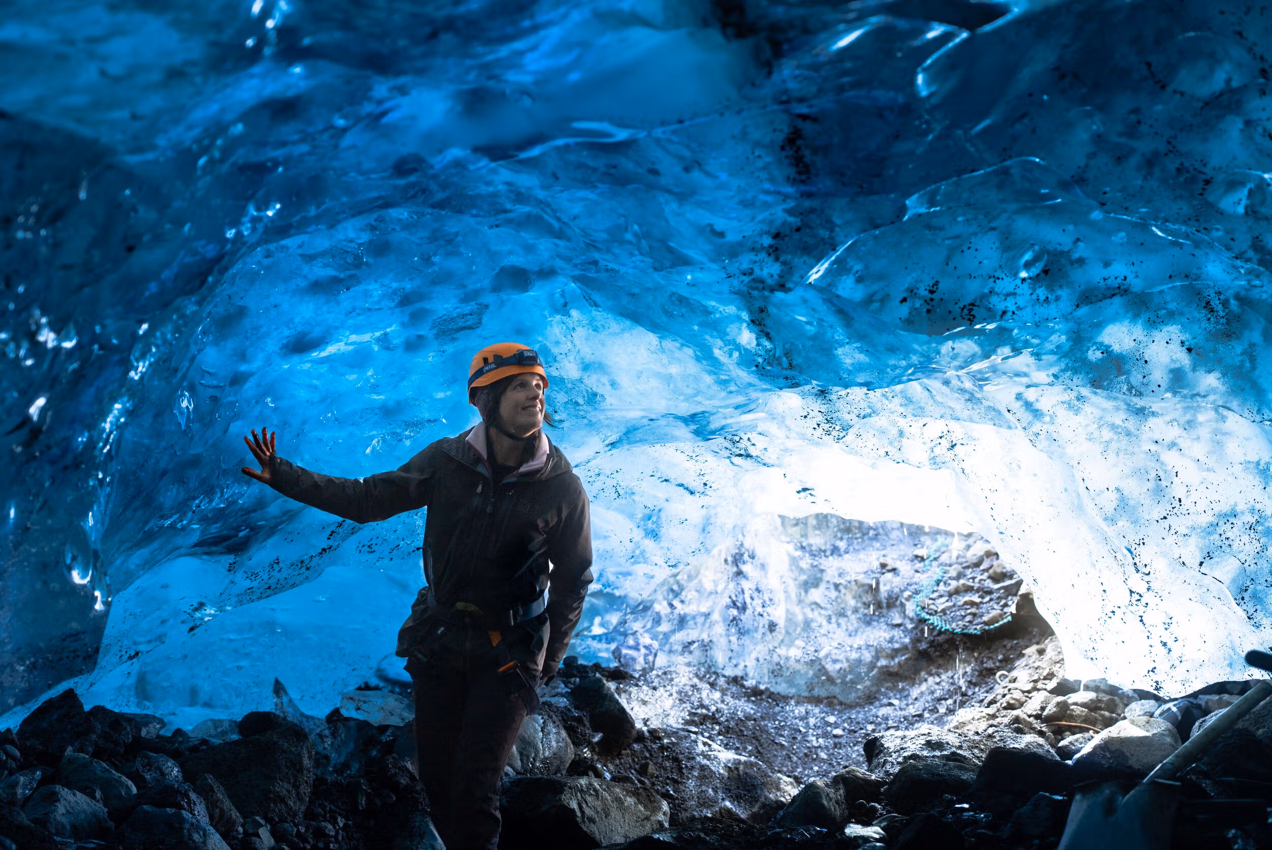 A helmeted visitor standing inside a blue ice cave on a glacier in Iceland.