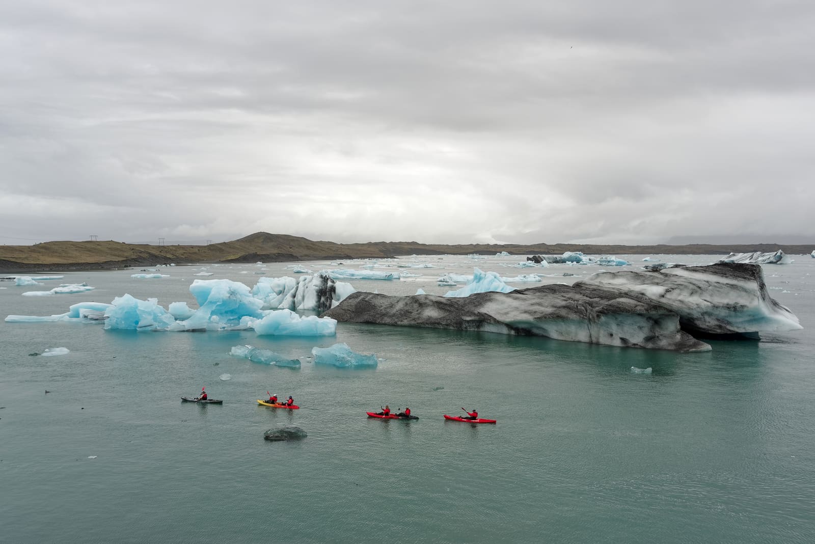 Guided kayakers crossing Jökulsárlón among blue and ash-striped icebergs