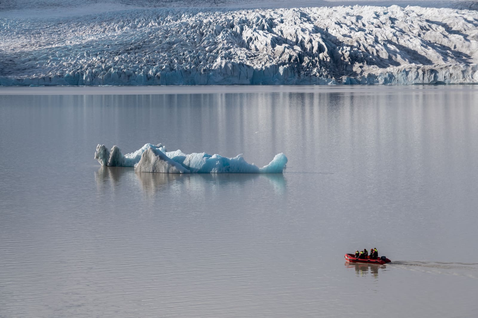 Small red Zodiac crossing calm water below the glacier at Jökulsárlón