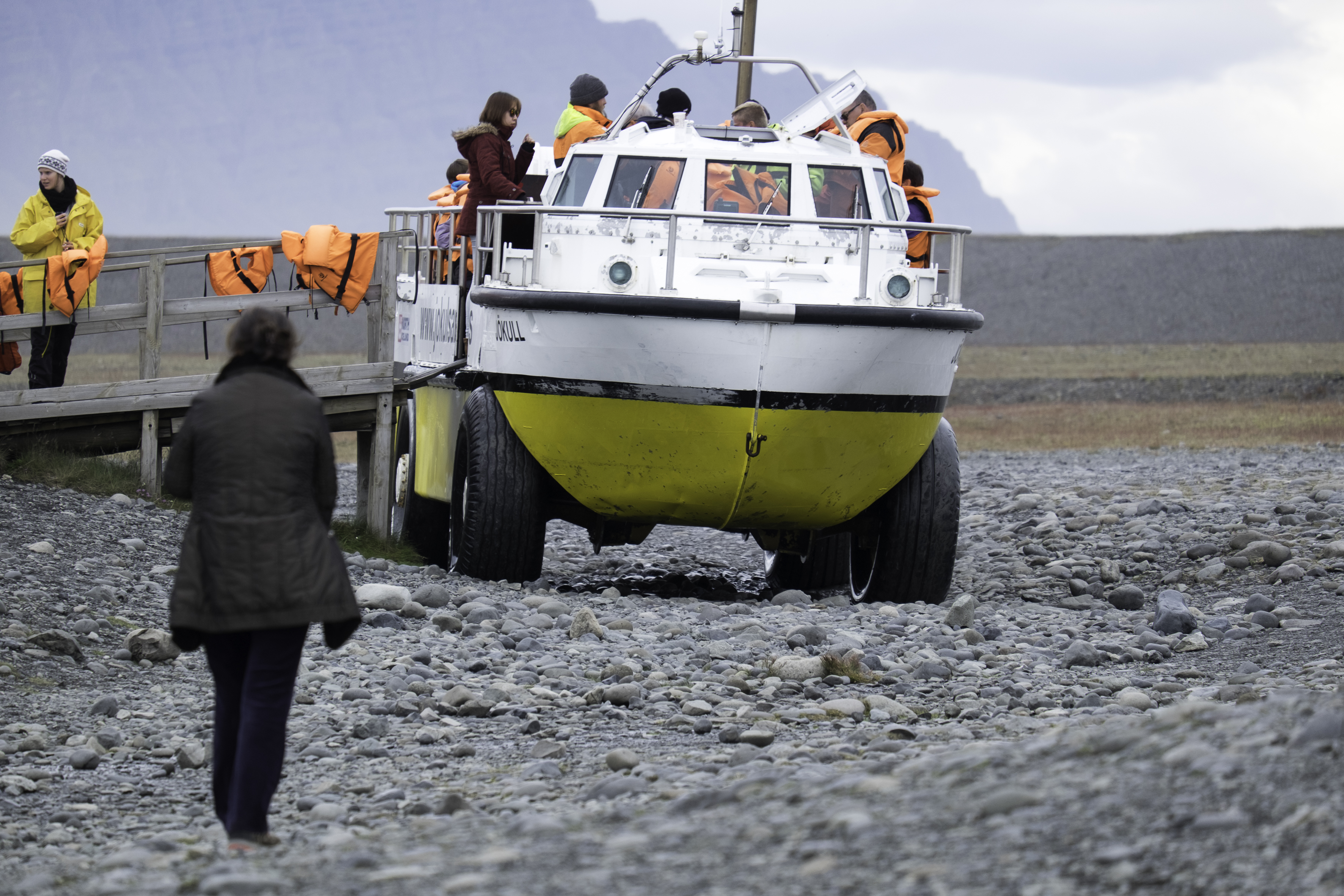 Passengers boarding a wheeled amphibian boat on the gravel shore at Jökulsárlón