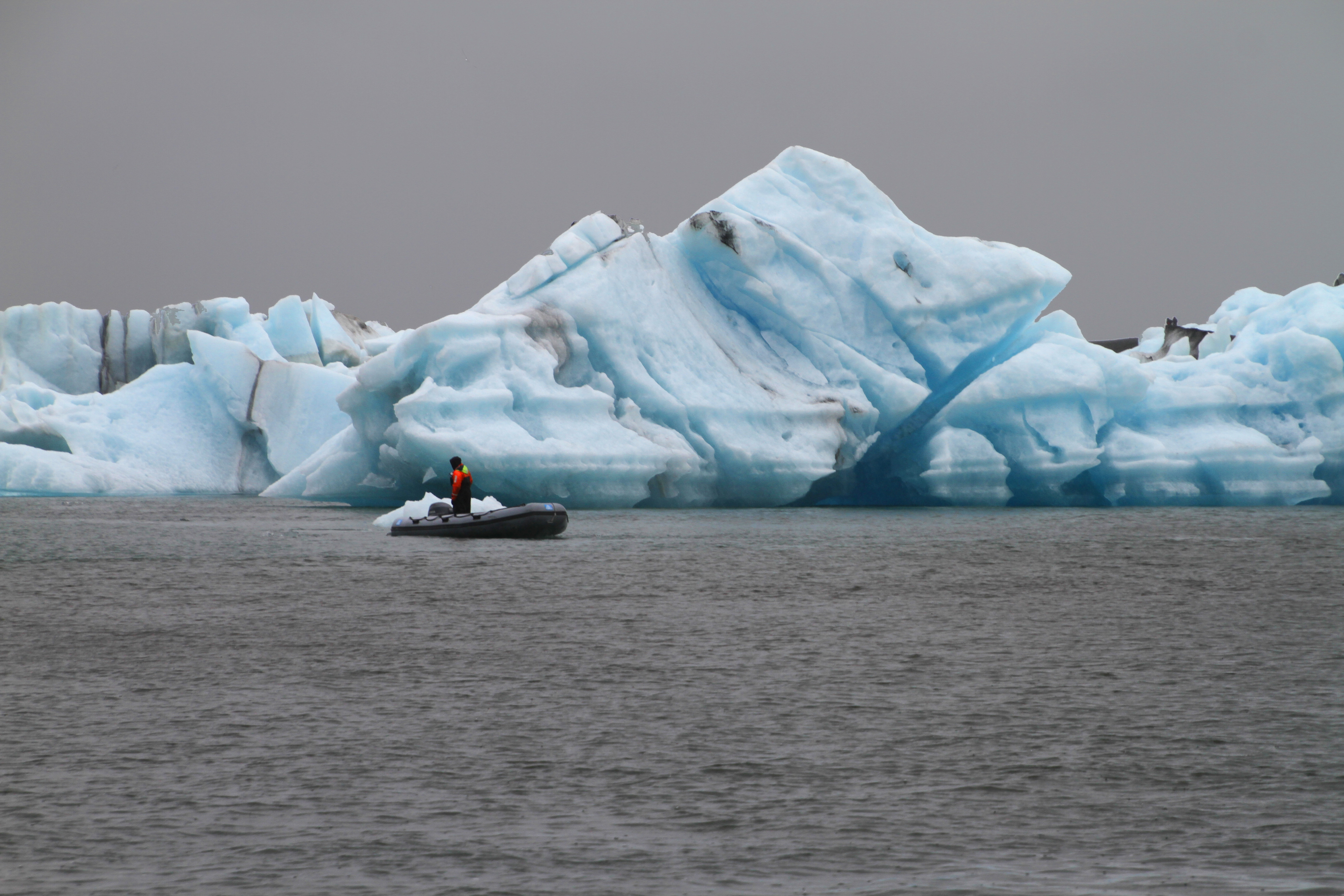 A guide in a small Zodiac beside a towering blue iceberg at Jökulsárlón