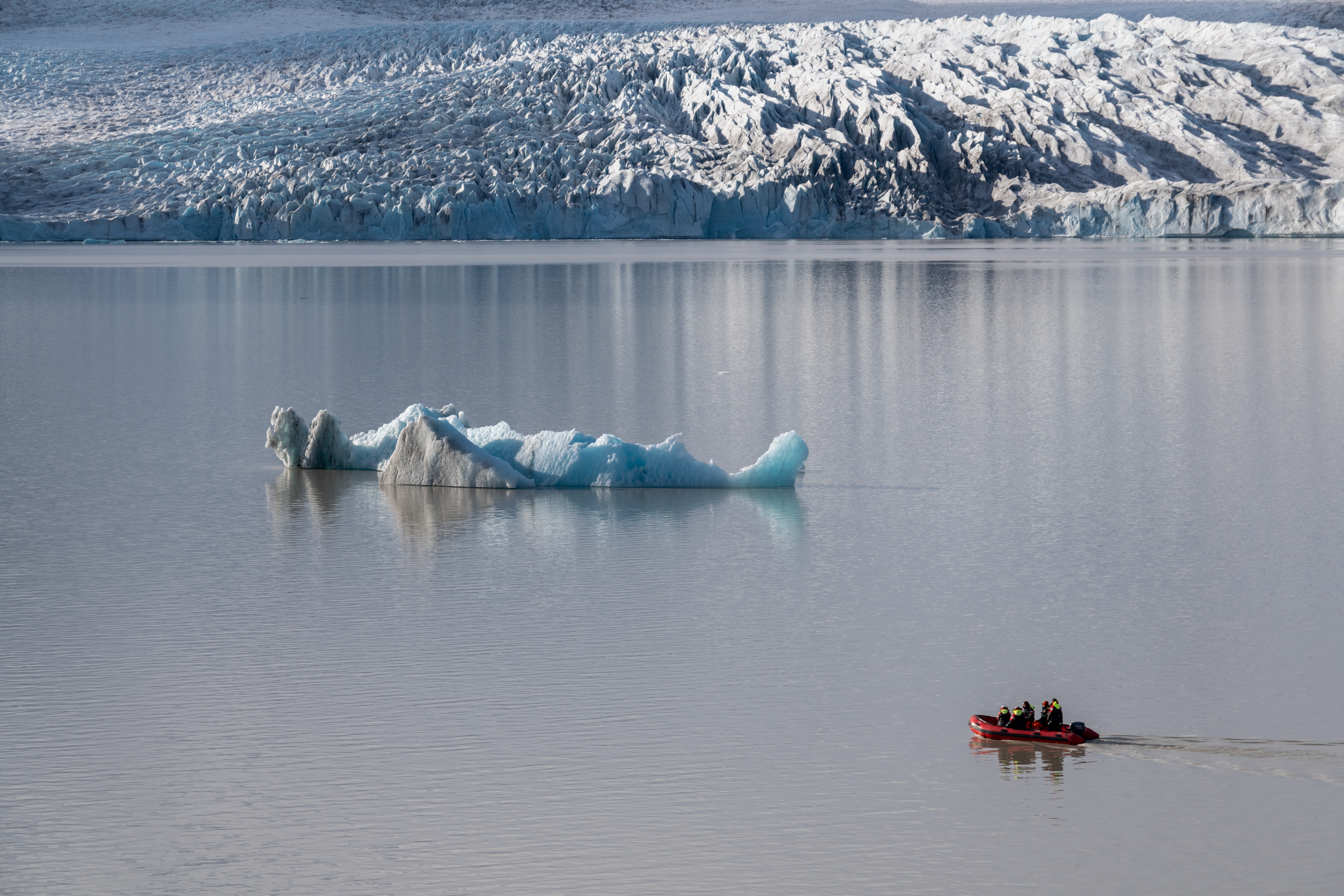 Small red Zodiac crossing calm water below the glacier at Jökulsárlón