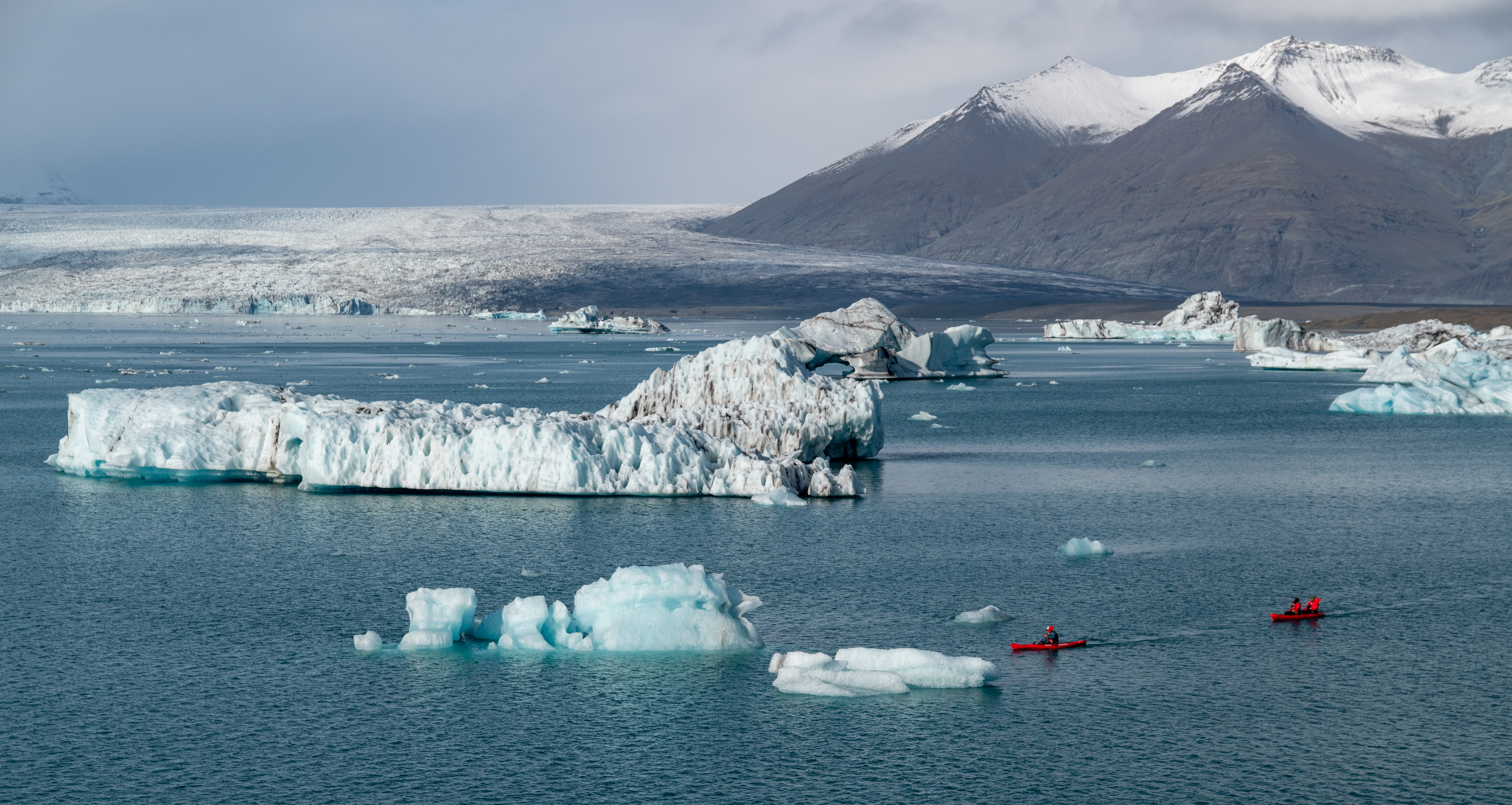 Red kayaks moving between icebergs beneath the glacier at Jökulsárlón