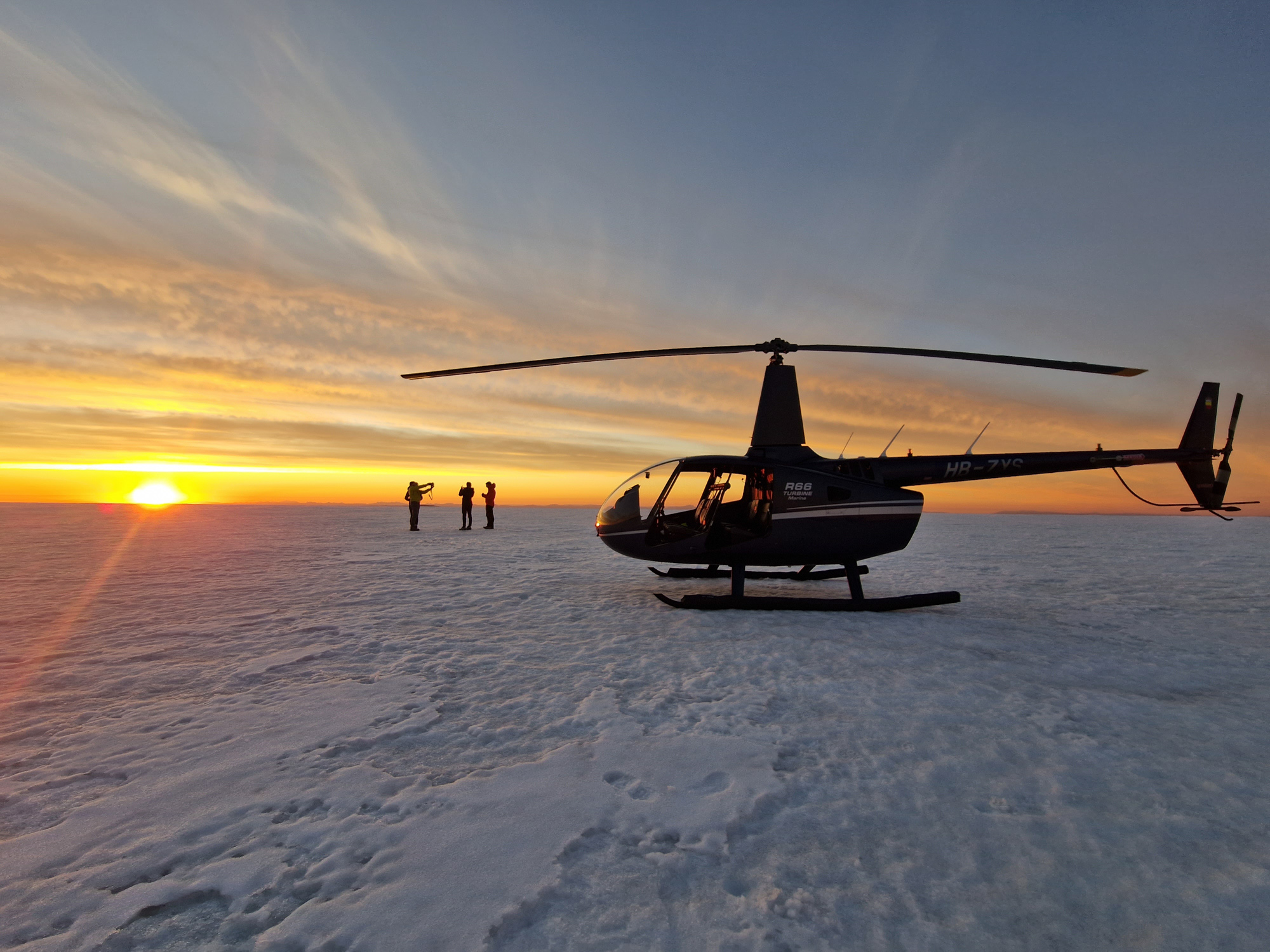 Travelers standing beside a helicopter during a low-light landing on an Icelandic glacier.