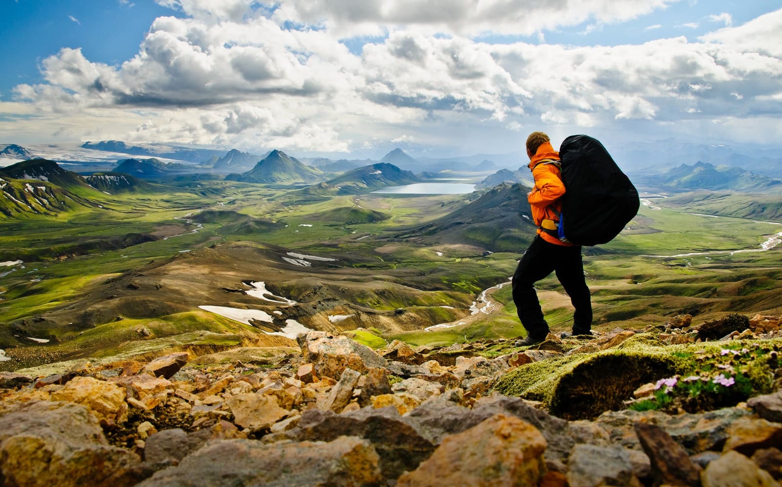Hiker overlooking green Icelandic highland valleys from a rocky ridge.