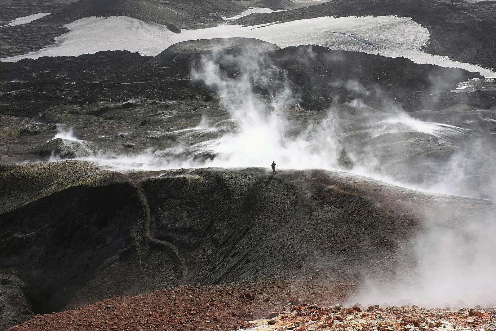 A lone hiker on the steaming volcanic pass of Fimmvorduhals between snowy glacier edges.