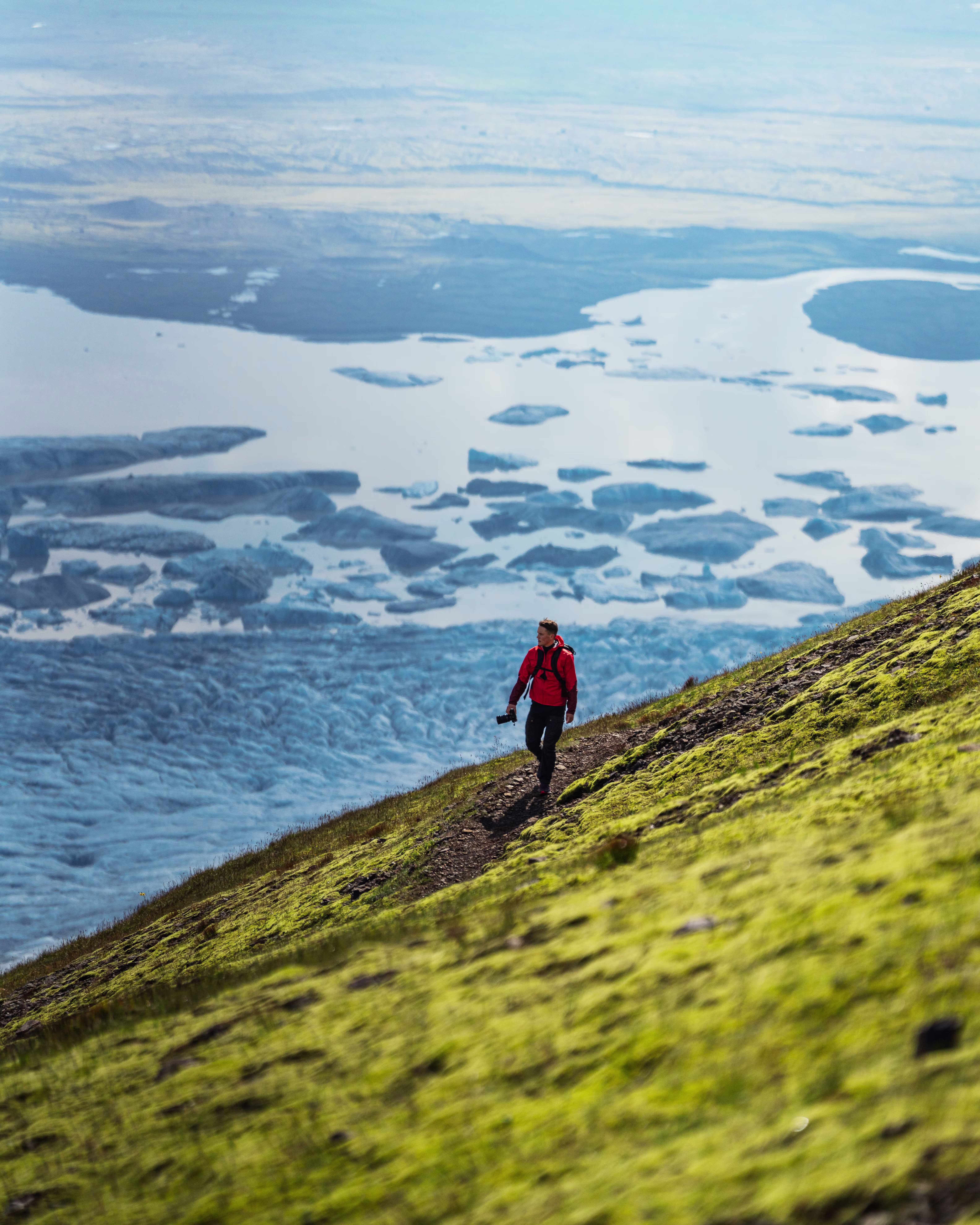 Walker on a Skaftafell trail above blue glacier ice and mossy slopes.