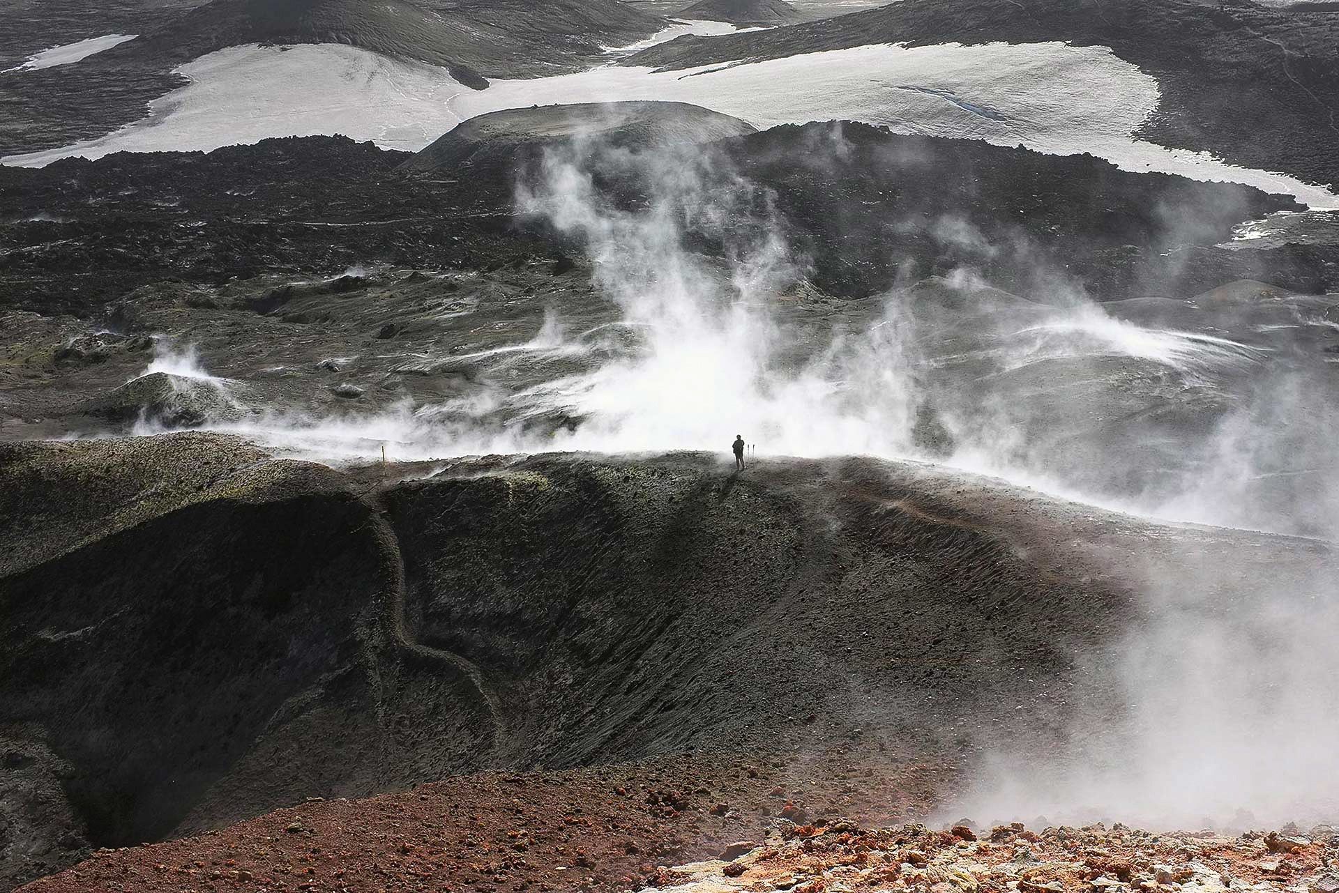 A lone hiker on the steaming volcanic pass of Fimmvorduhals between snowy glacier edges.