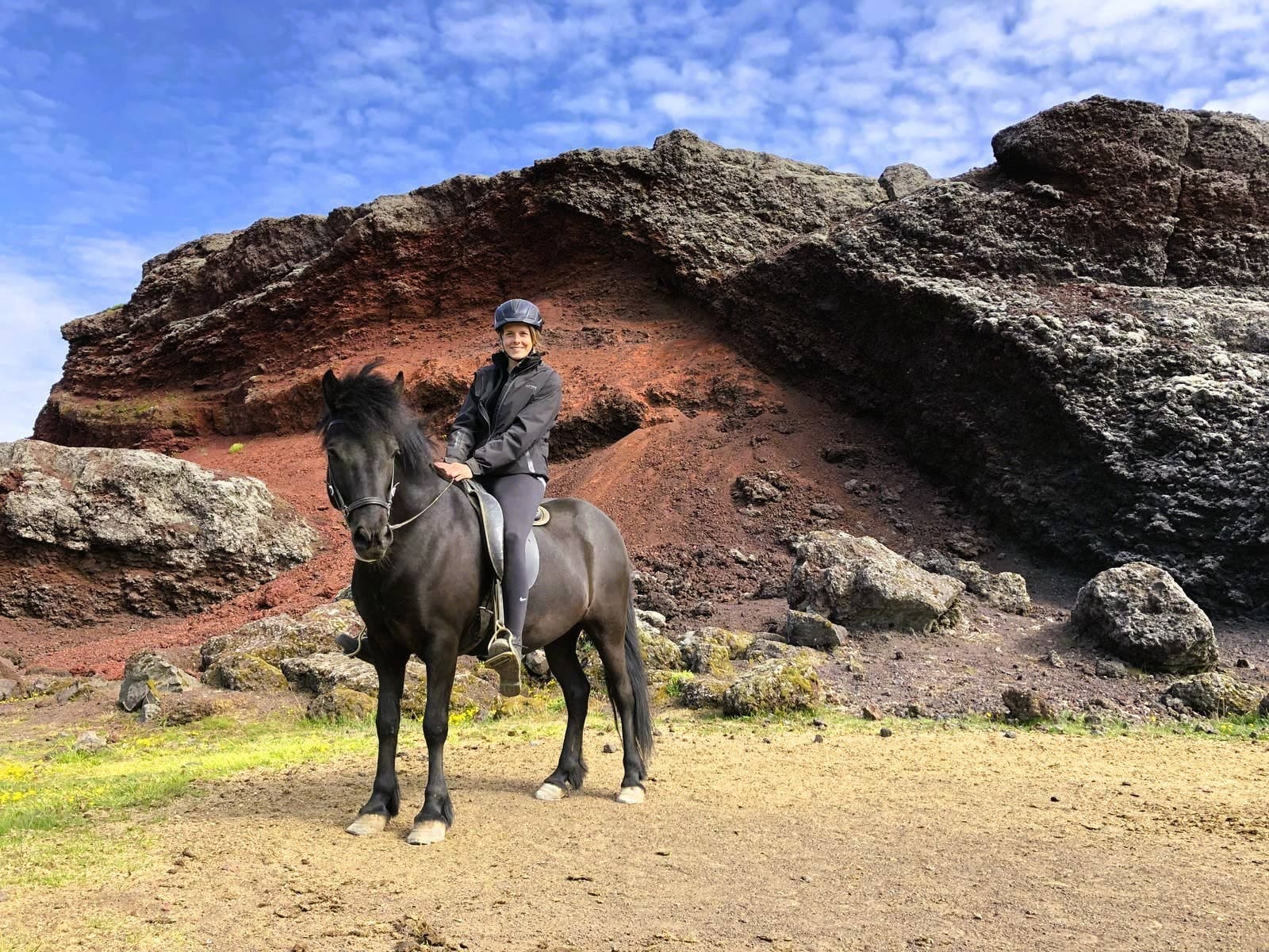 A rider on an Icelandic horse moving through open volcanic countryside.