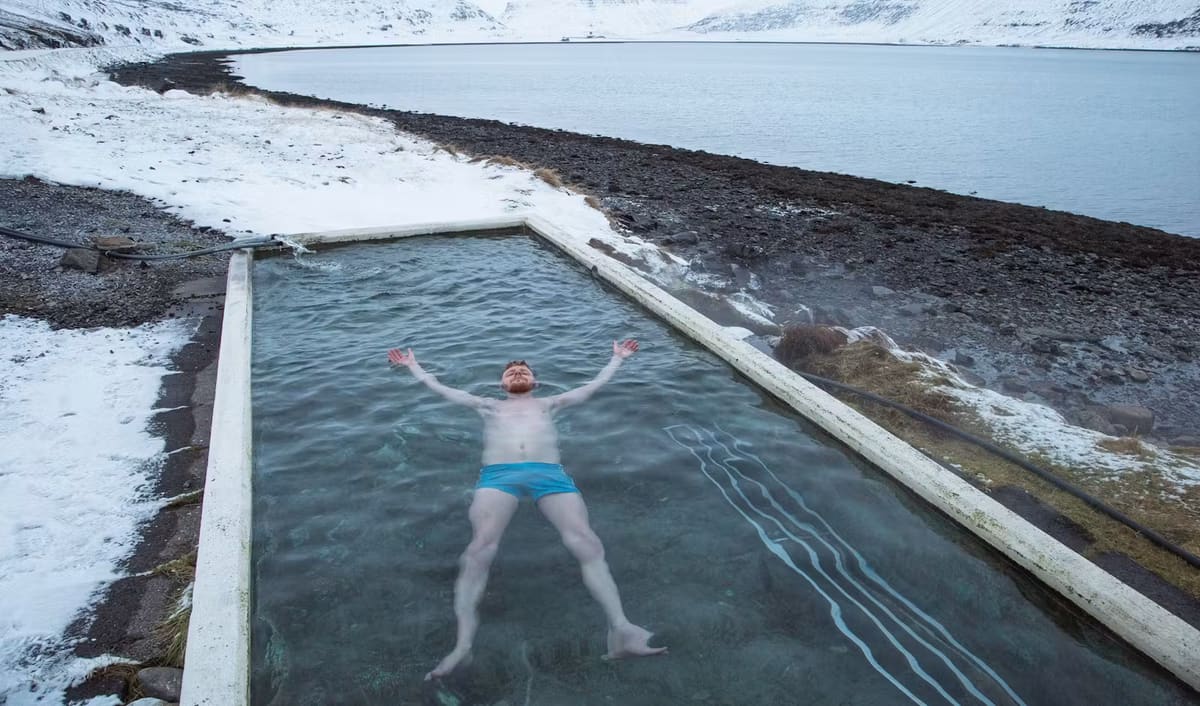 A swimmer relaxing in a warm Icelandic pool with mountain scenery beyond