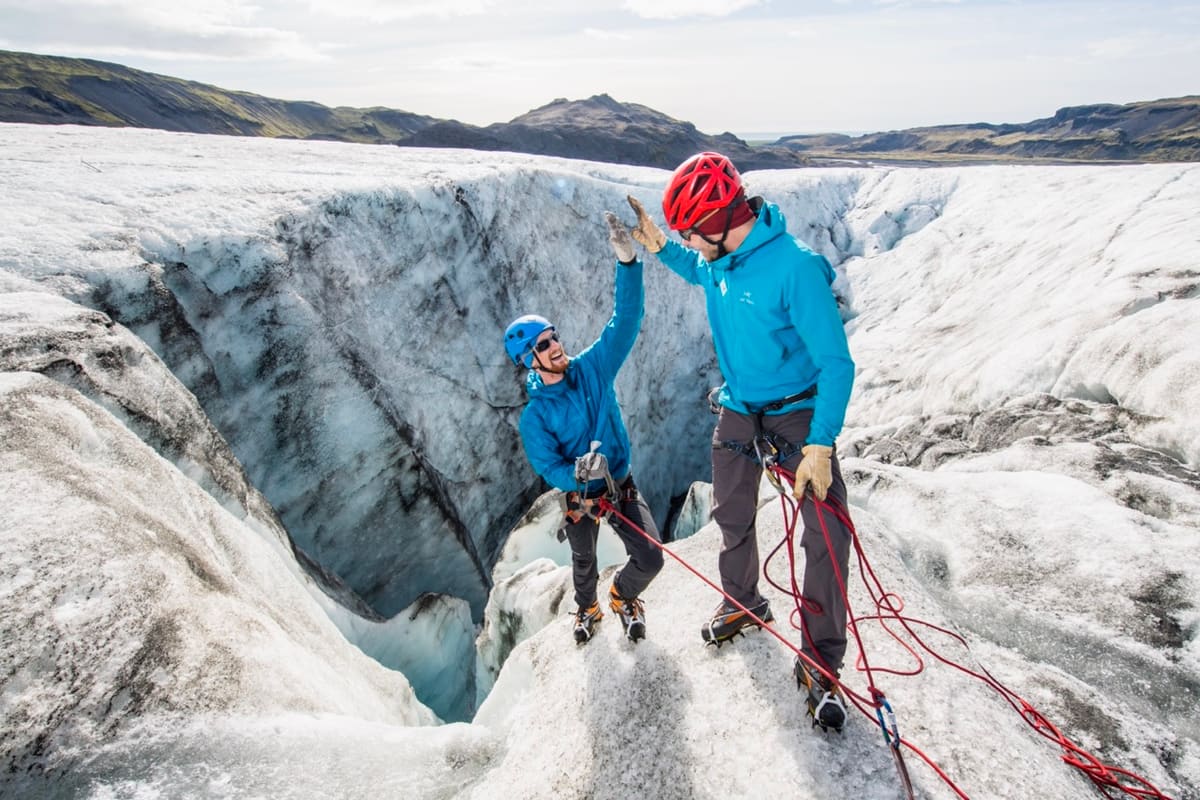 Two helmeted climbers handling ropes beside an open glacier crevasse