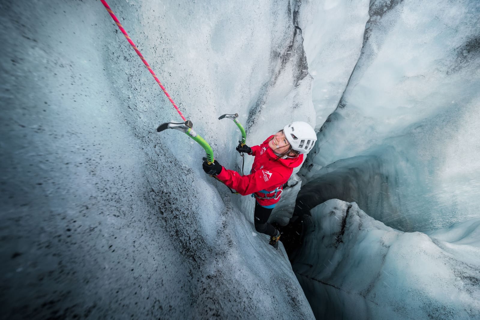Roped ice climber in a red jacket ascending a narrow glacier wall in Iceland