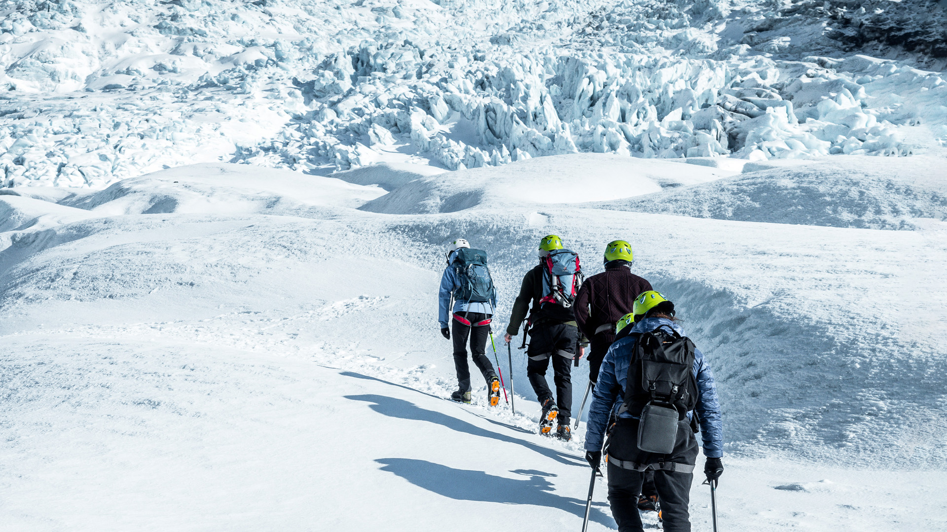 Small group in helmets walking across a glacier toward a steep icefall