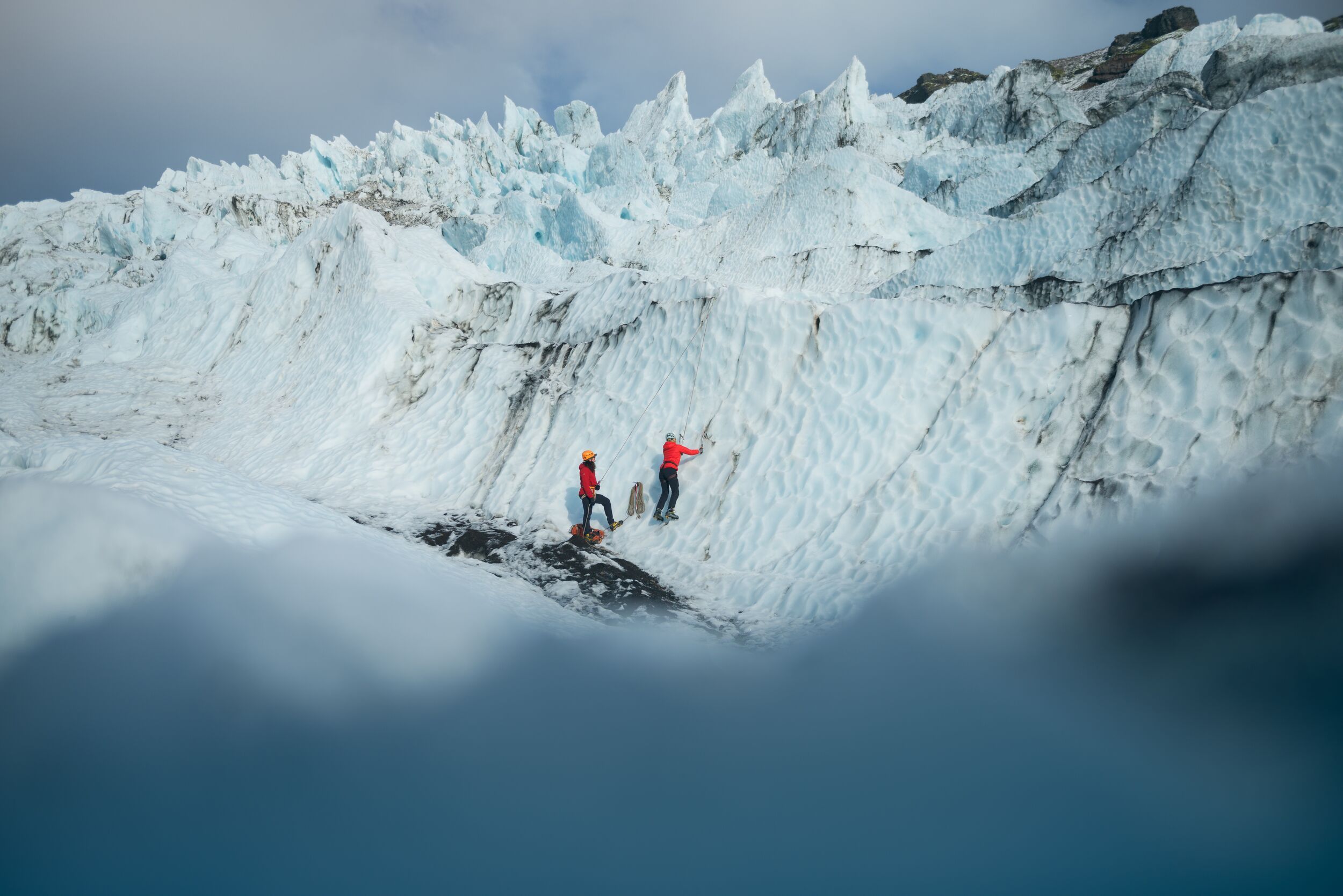 Two climbers in bright jackets using different parts of a steep glacier ice feature