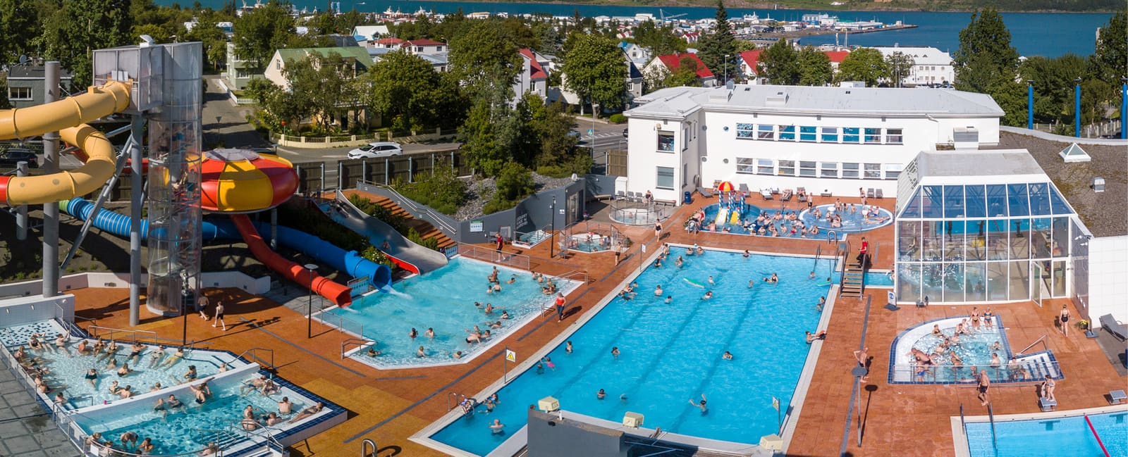 Aerial view of Akureyri Swimming Pool with lane pools, hot tubs, slides, and the town beyond