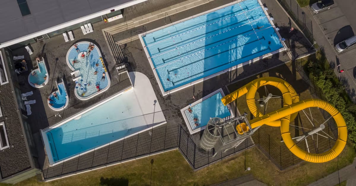 Overhead view of Álftaneslaug with lane pools, shallow water, hot tubs, and a yellow waterslide