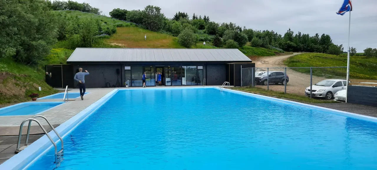 Hreppslaug’s service building, outdoor swimming pool, and hot-water area below a green hillside