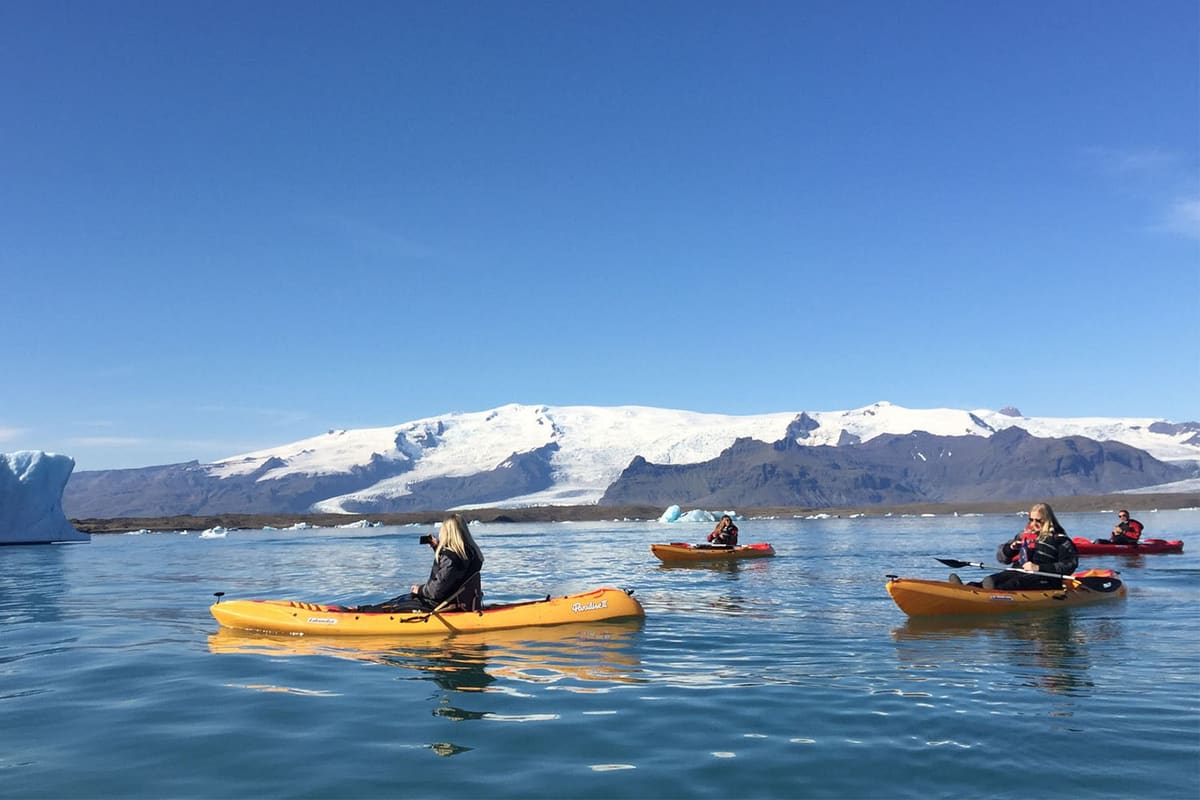 Several kayakers crossing calm blue water with a broad Icelandic glacier behind them