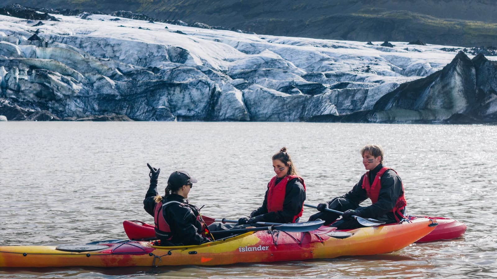 Kayak guide speaking to two paddlers seated low on a glacier lagoon