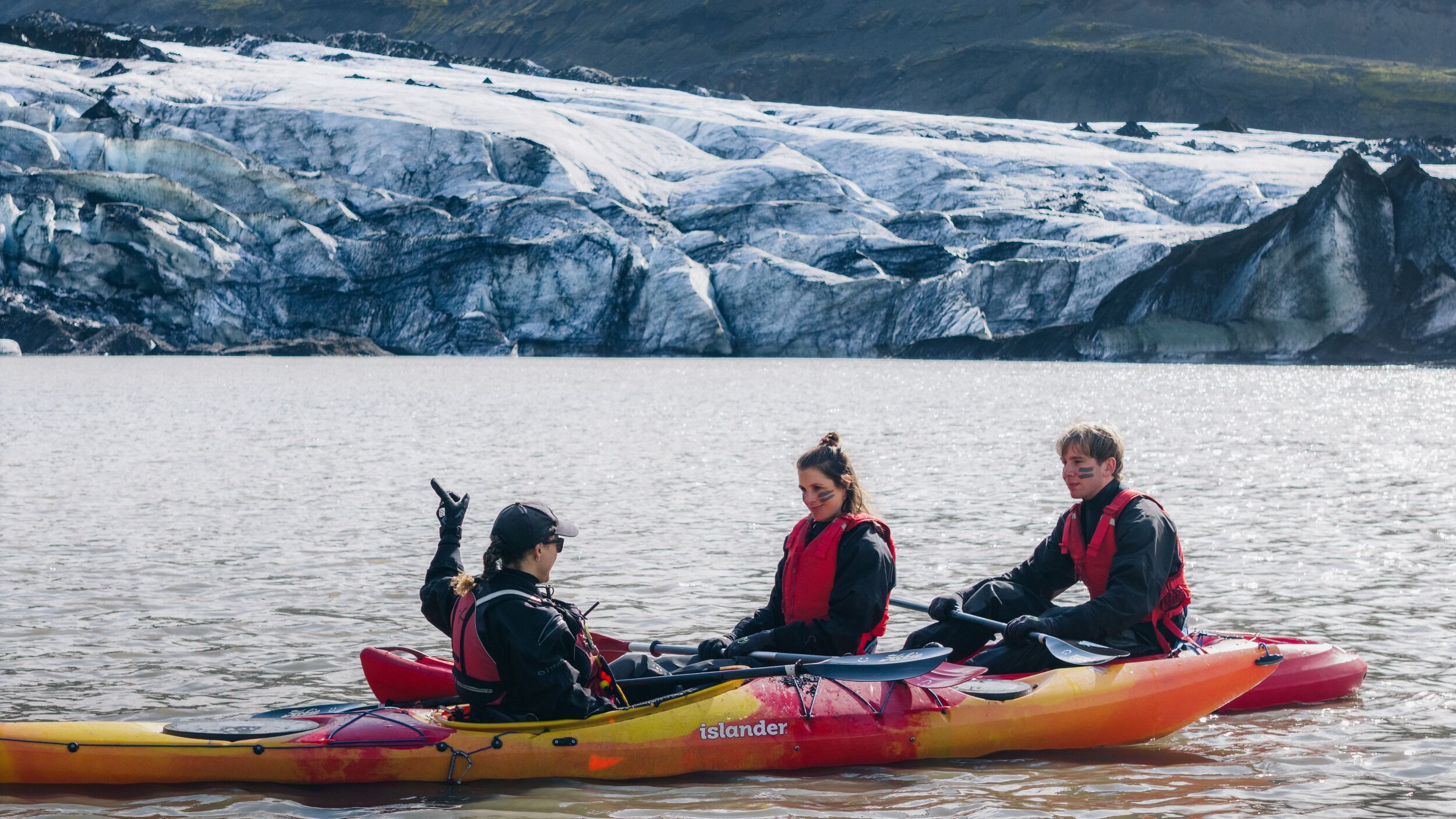 Kayak guide speaking to two paddlers seated low on a glacier lagoon