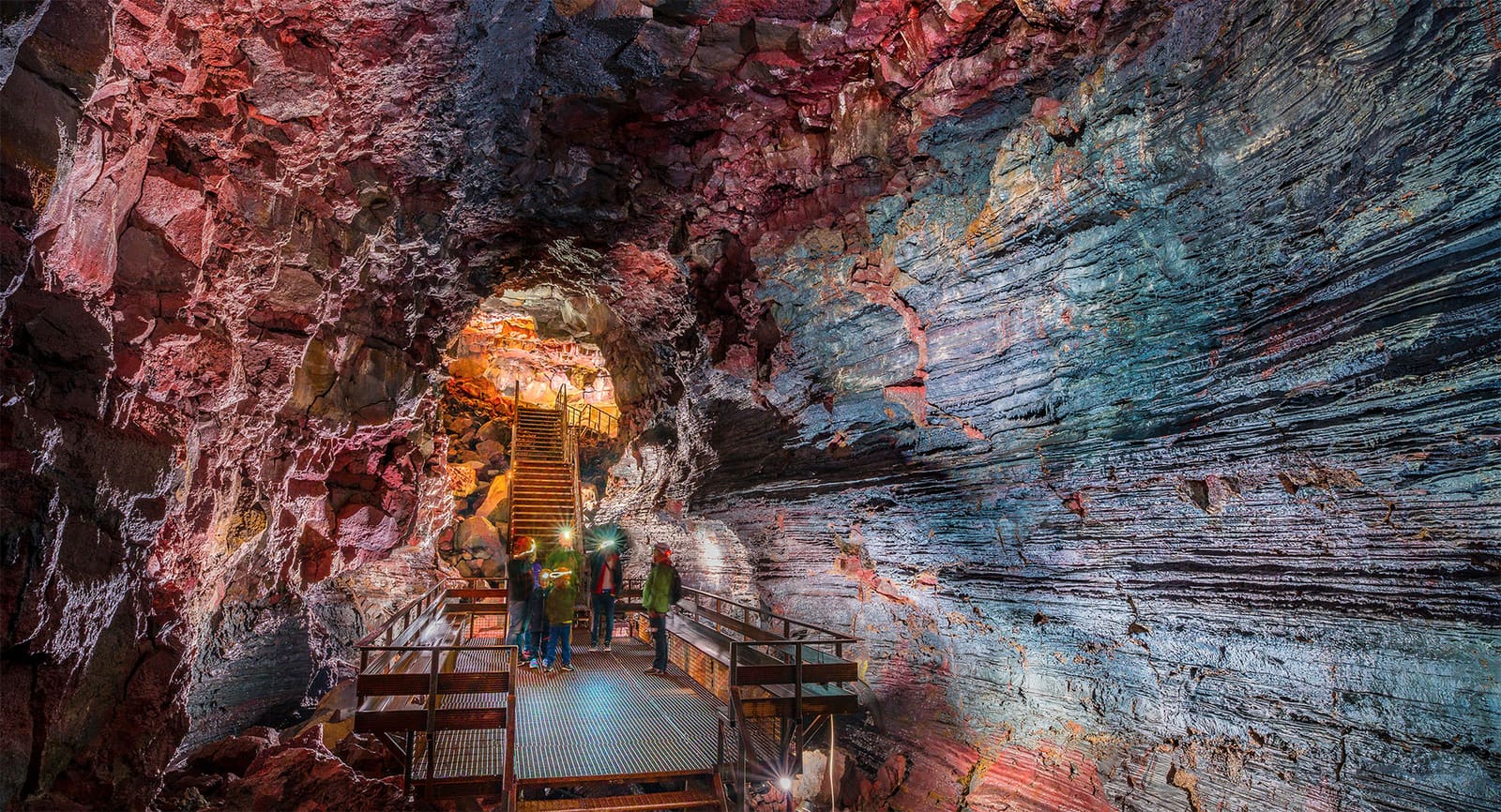 Visitors standing on a metal platform inside the layered basalt walls of Raufarhólshellir lava tunnel