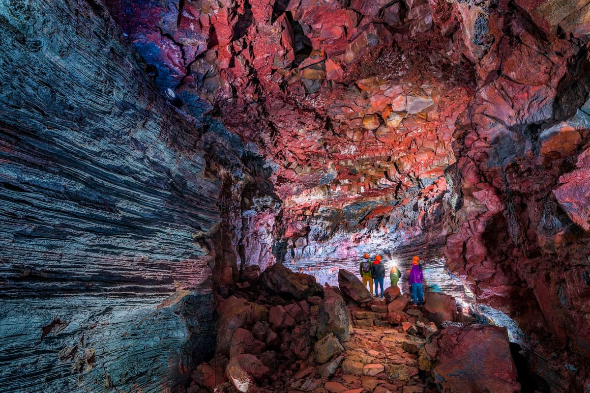 Helmeted visitors walking over rough lava rock inside the colorful walls of Raufarhólshellir