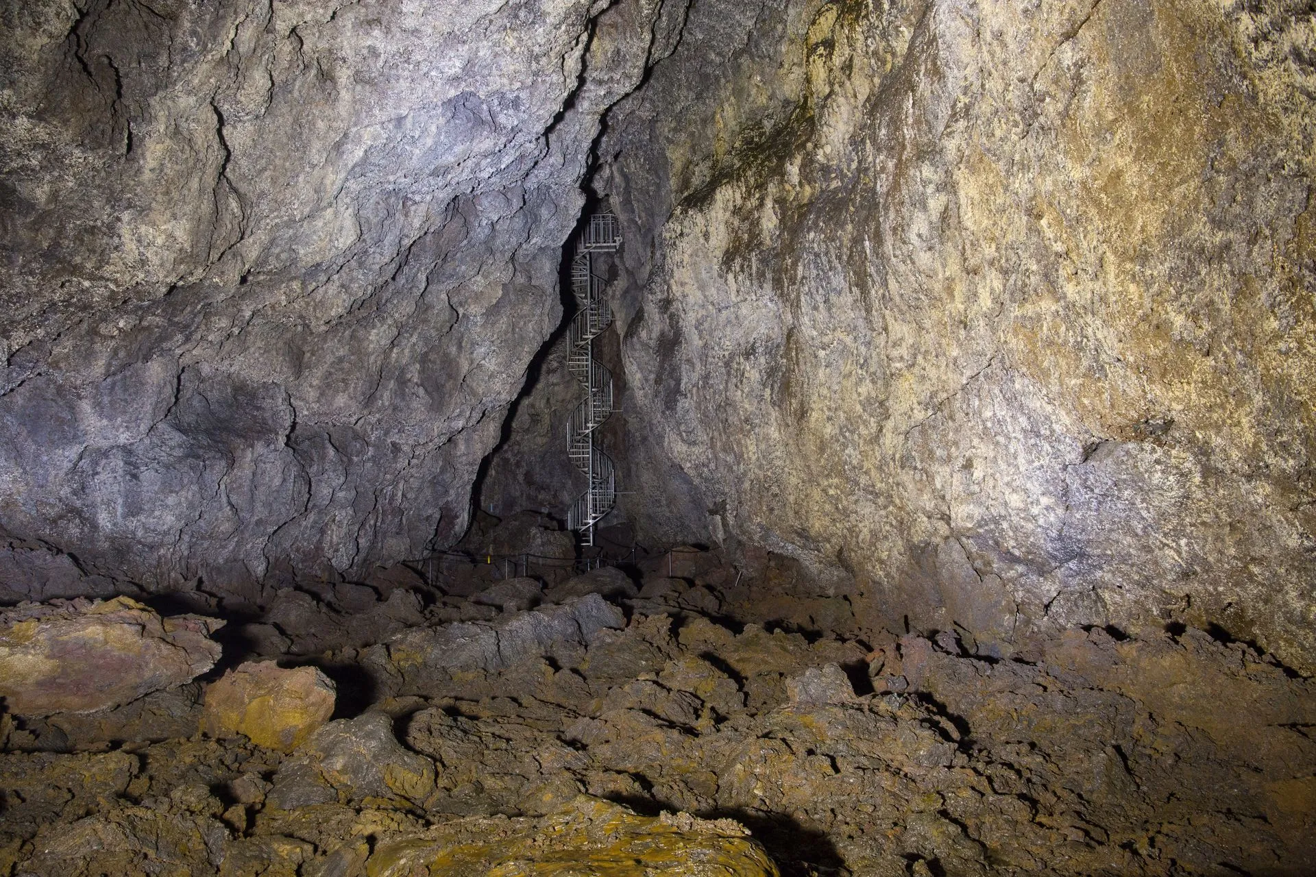 Metal spiral staircase descending between rough lava walls inside Vatnshellir Cave