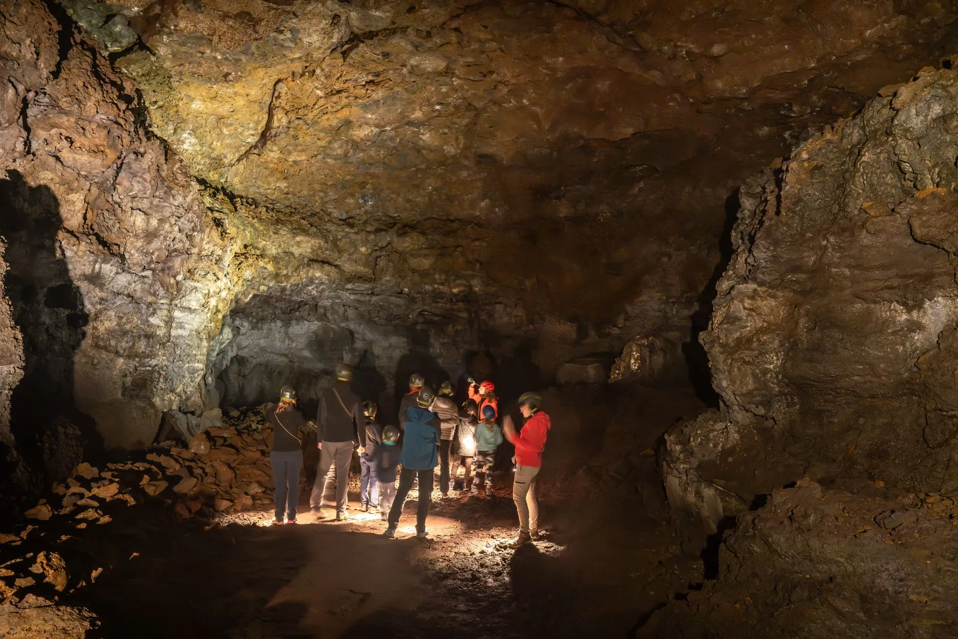 Guided visitors wearing helmets and using lights on the uneven floor inside Vatnshellir Cave
