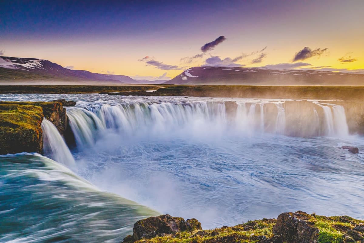 Goðafoss waterfall flowing below mountains in low yellow summer light