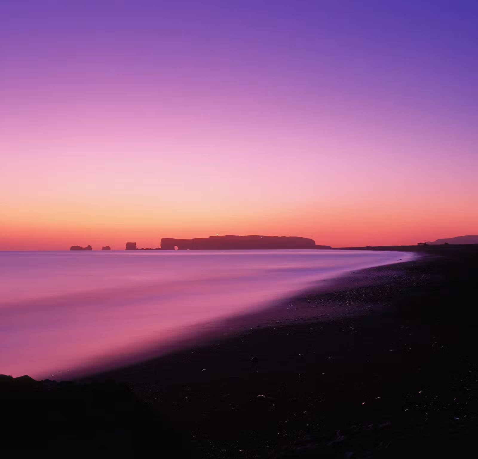 Pink low light over the black sand coast and sea arch at Dyrhólaey