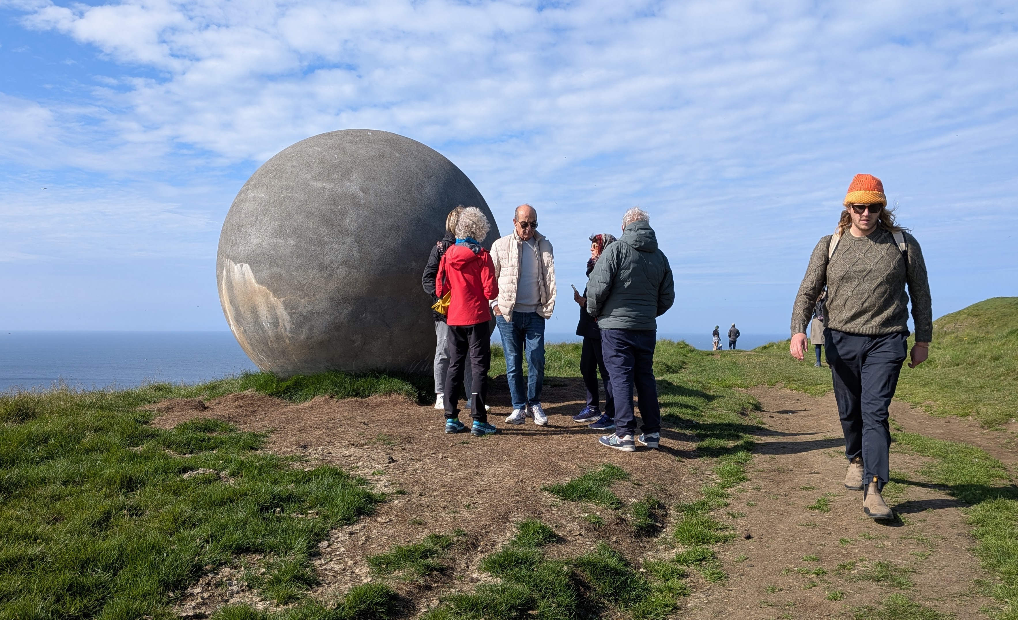 Visitors beside the Orbis et Globus Arctic Circle sphere on grassy Grímsey